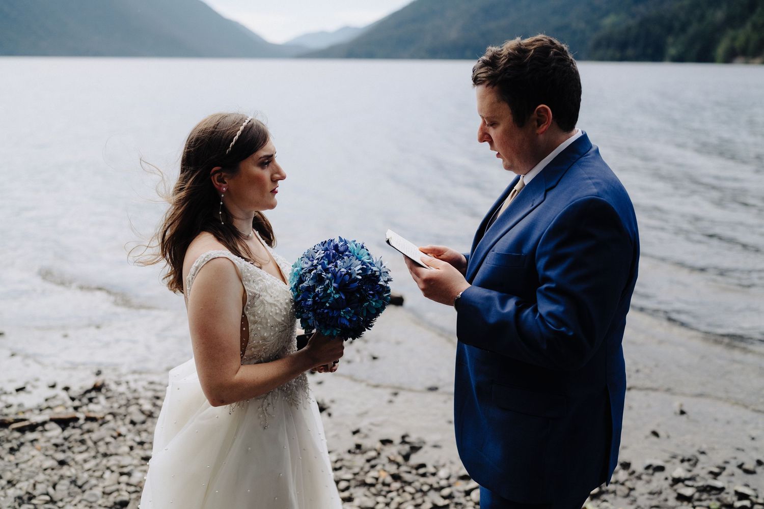 Intimate wedding ceremony on a rocky lake shore with mountains in the background and blue hydrangea bouquet.
