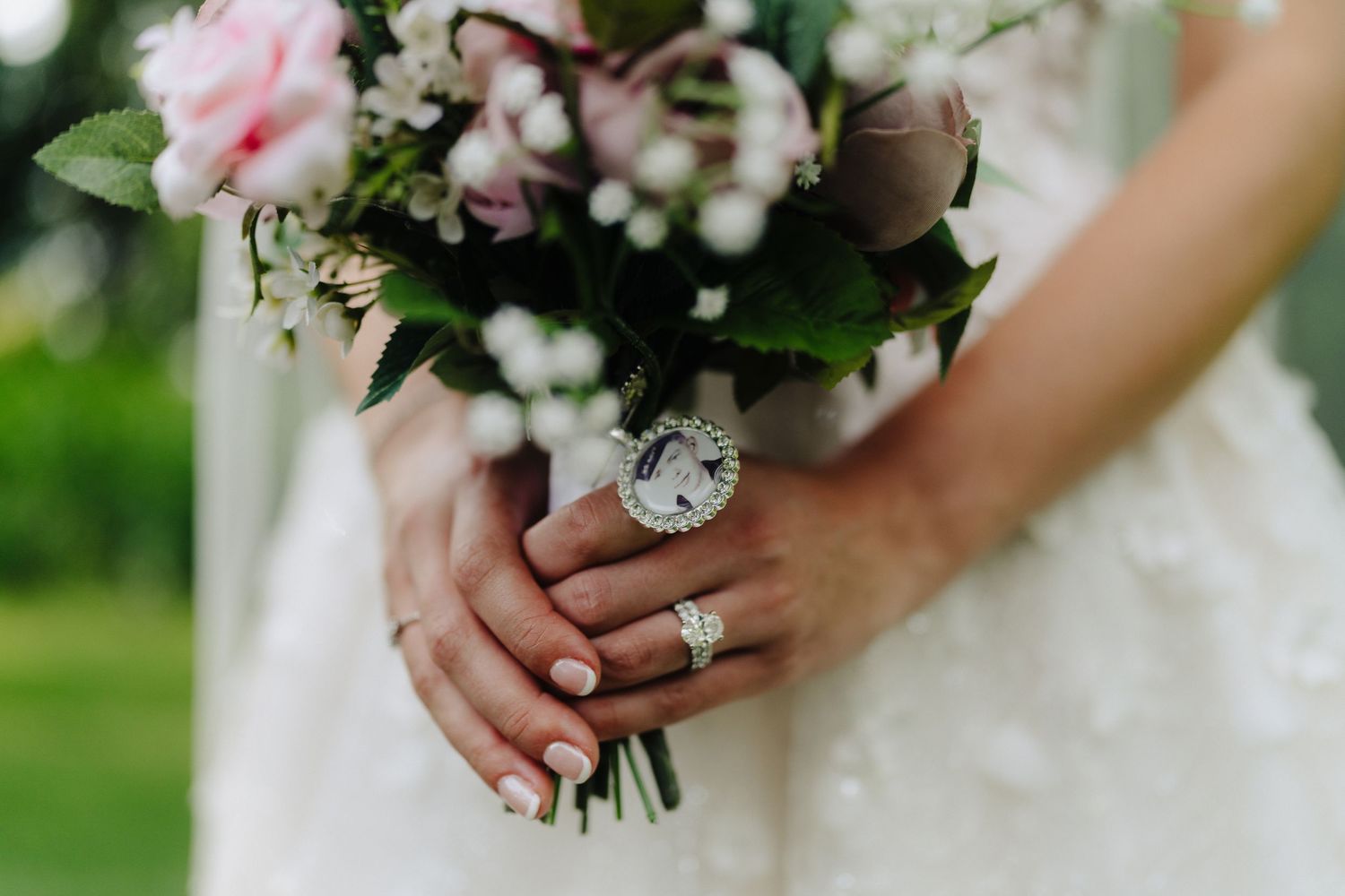 Elegant wedding bouquet with pink and white flowers held against a white dress.