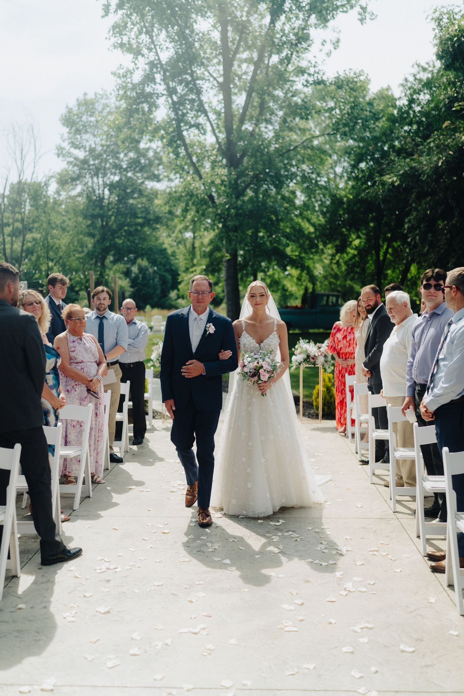 Wedding ceremony processional on white chairs with guests watching along the aisle.