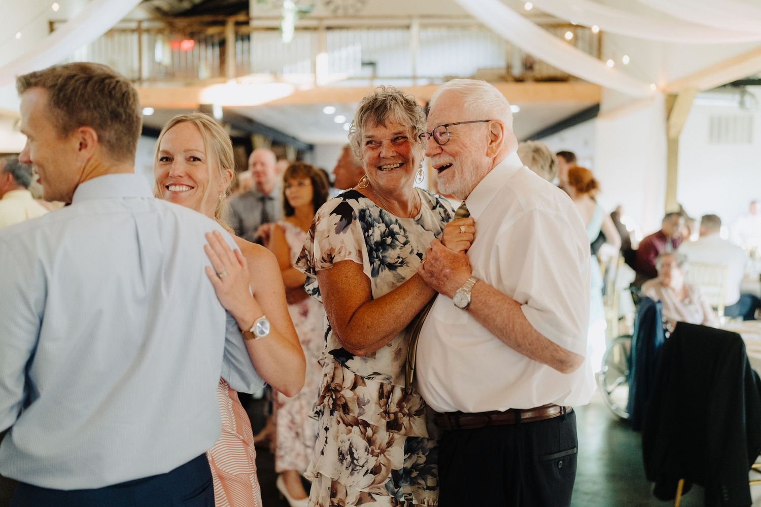 Wedding reception guests dancing and laughing under white tent covering.