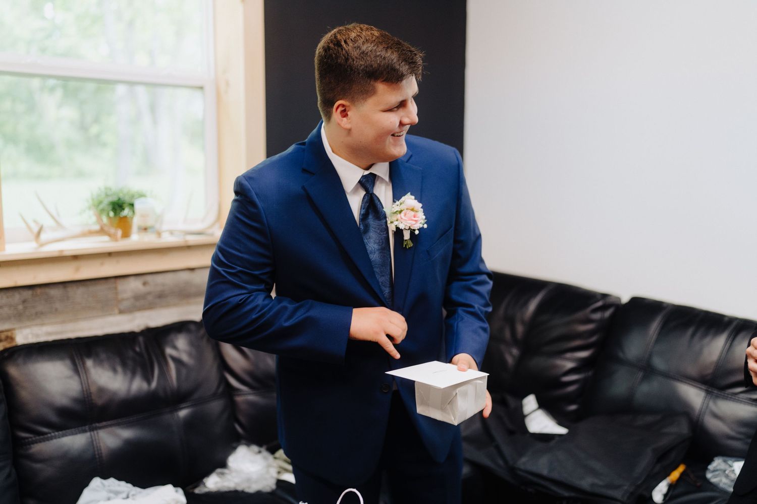 A person in a navy blue suit sits on a black leather couch reading a letter.