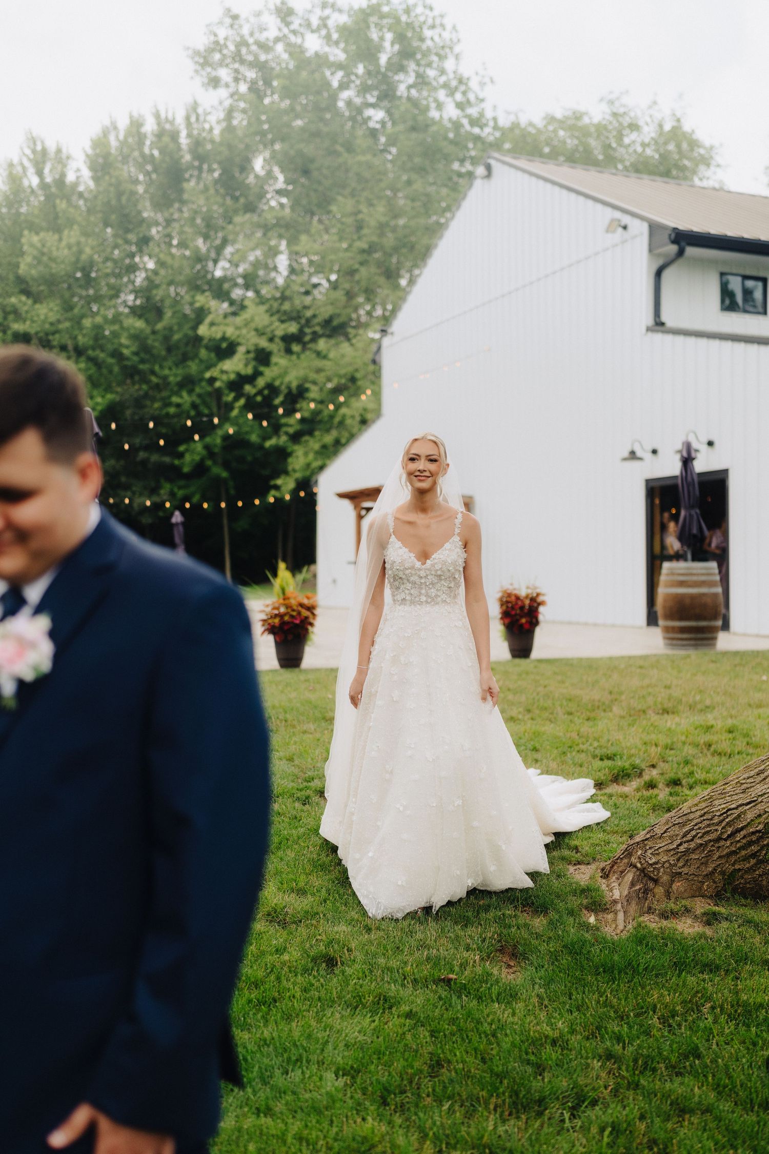 Outdoor wedding ceremony setup with white barn and string lights creating a rustic backdrop.