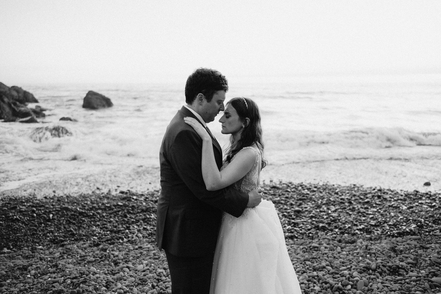 A romantic moment captured in black and white on a rocky beach.