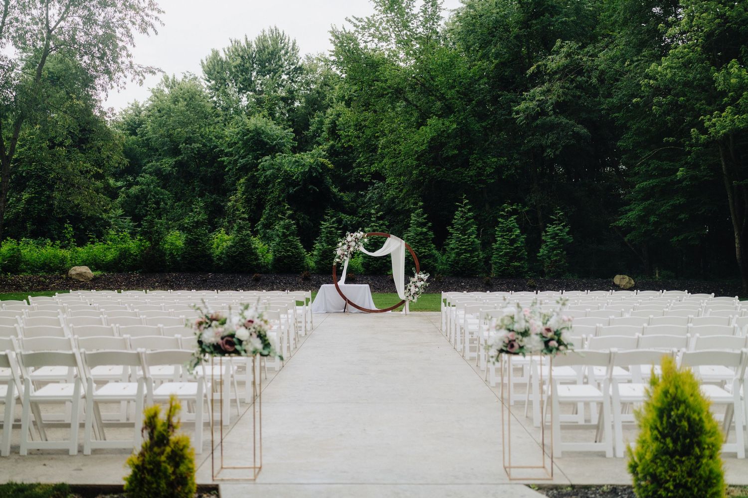 Outdoor wedding ceremony setup with white chairs and floral arrangements in a lush garden setting.
