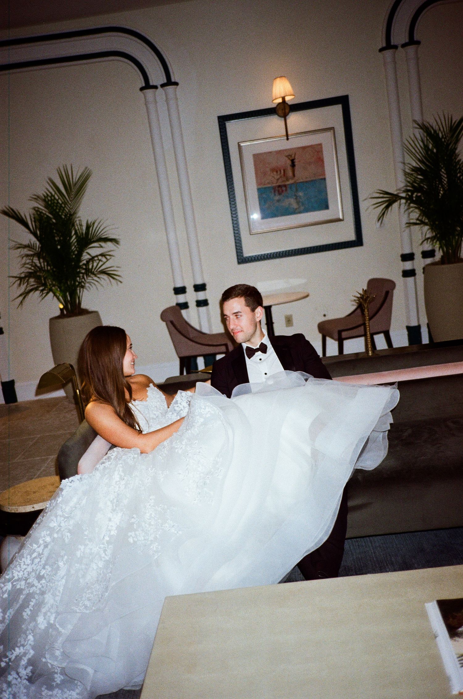 A person in a flowing white wedding dress lies across a couch in an elegant indoor setting.