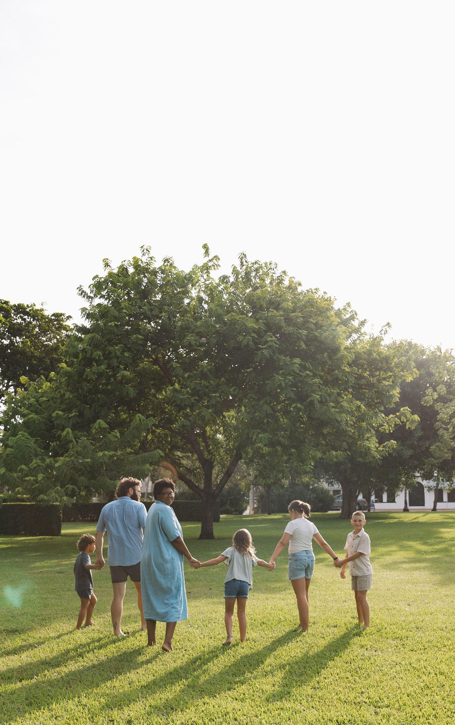 A group of people walking together on a sunny lawn with trees in the background during golden hour.