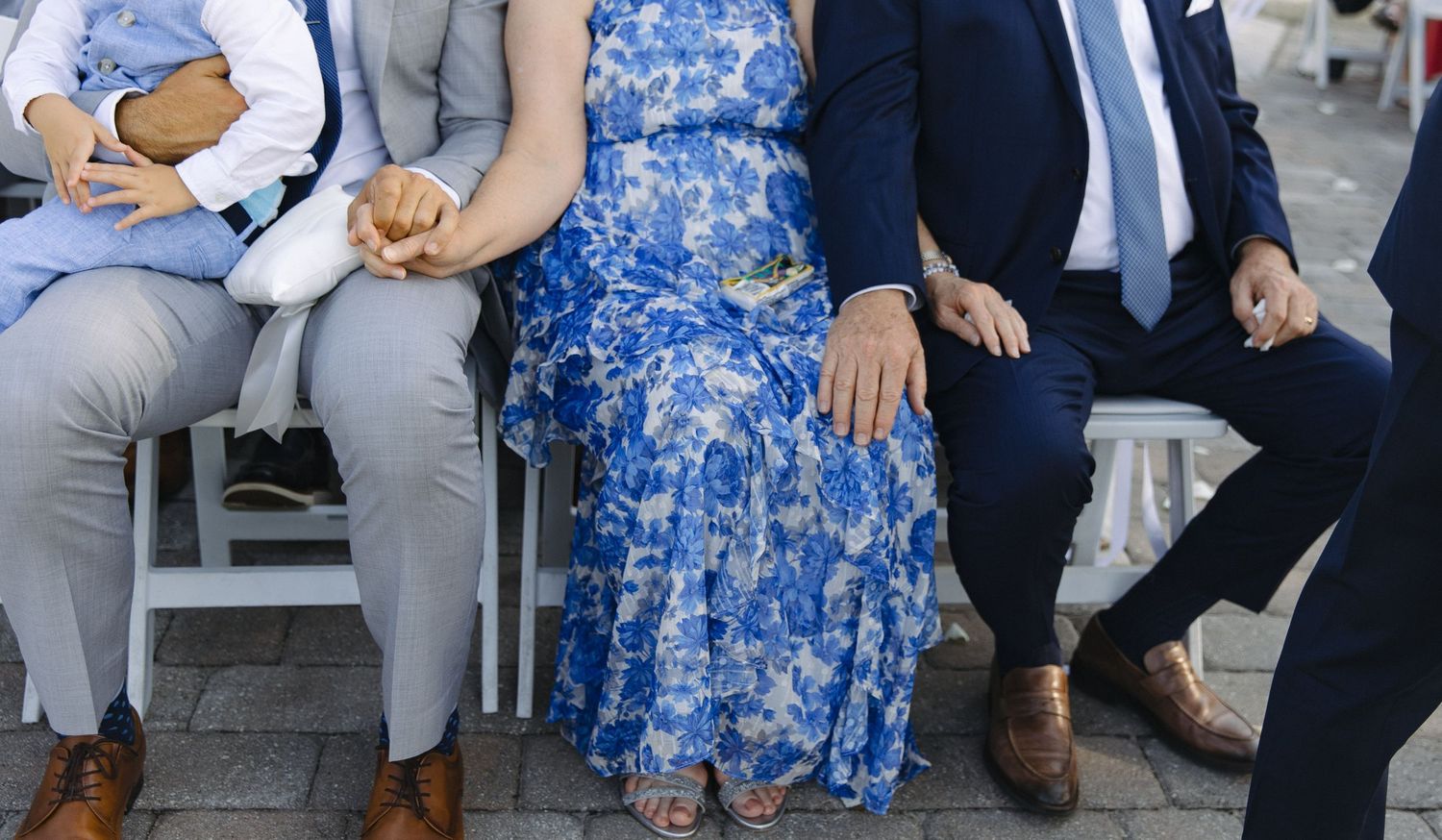 Wedding guests in blue dresses and formal attire seated outdoors during ceremony.