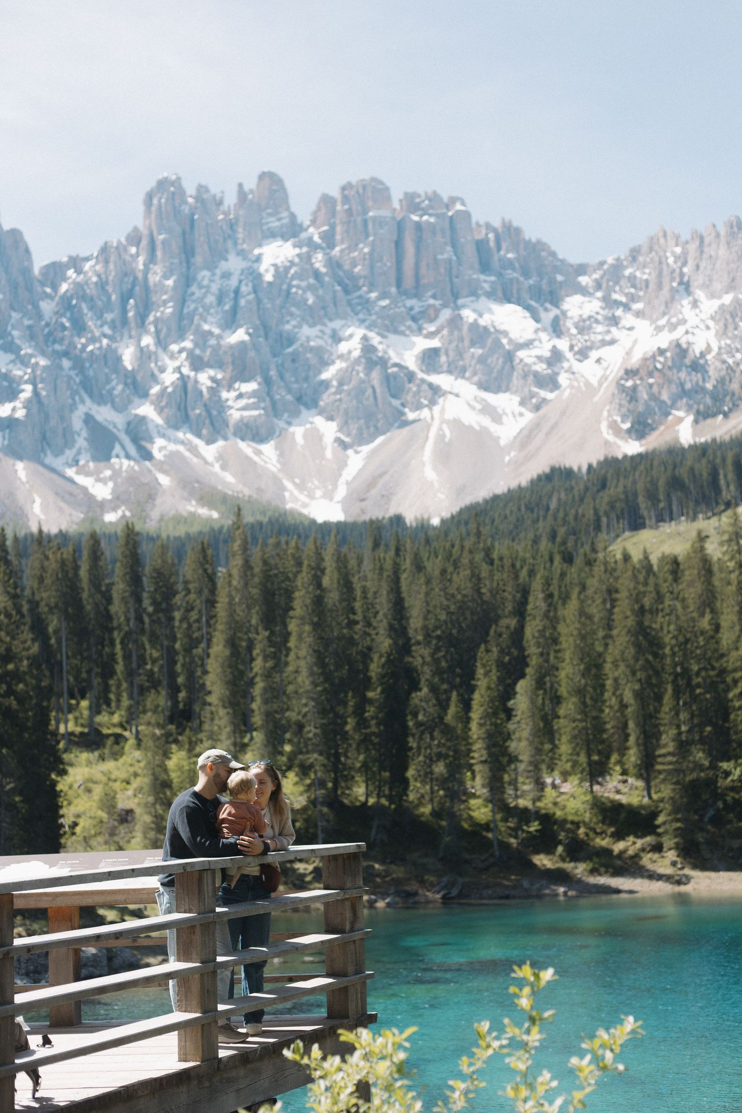 Alpine lake surrounded by snow-capped peaks and dense pine forest under blue sky.