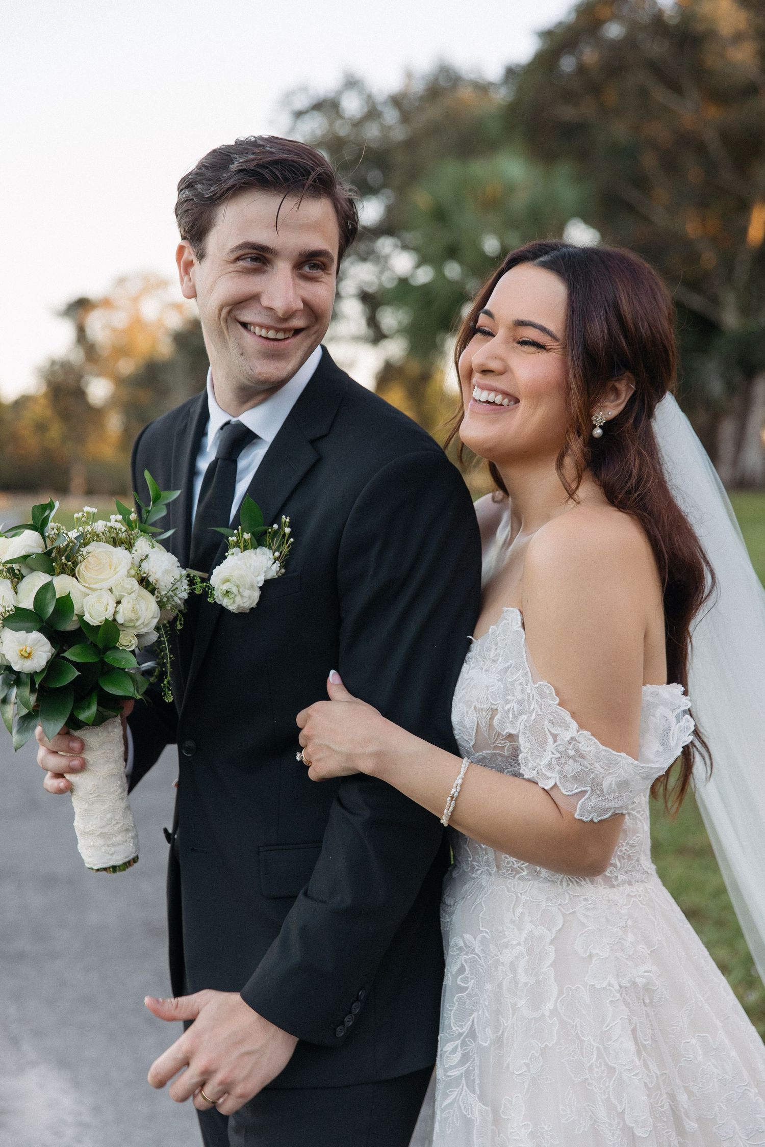 A newlywed couple shares joyful moments in their wedding attire against a natural outdoor backdrop.
