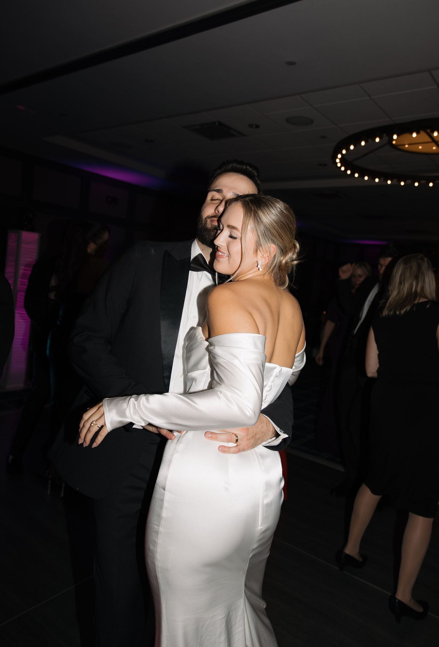 Romantic dance sequence of newlyweds in formal wear embracing on a dimly lit dance floor at their wedding reception.