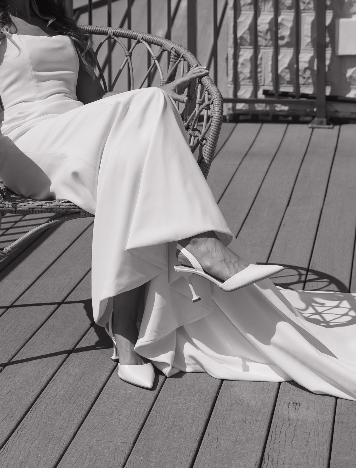 Black and white photo of an elegant white dress and heels on a wooden porch with ornate railing details.