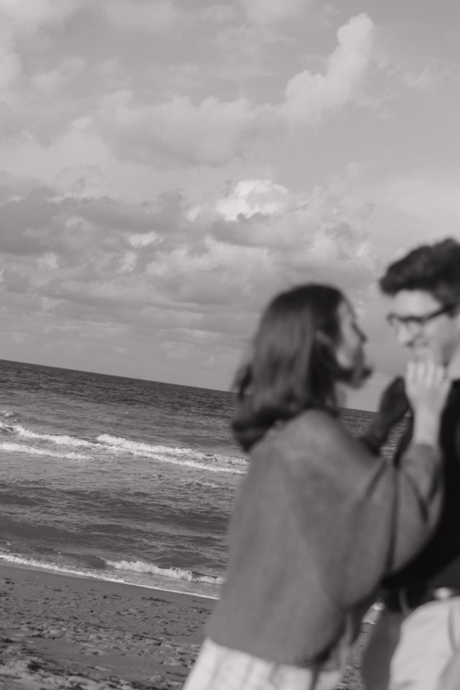 Black and white beach scene with couple sharing an intimate moment by the ocean.