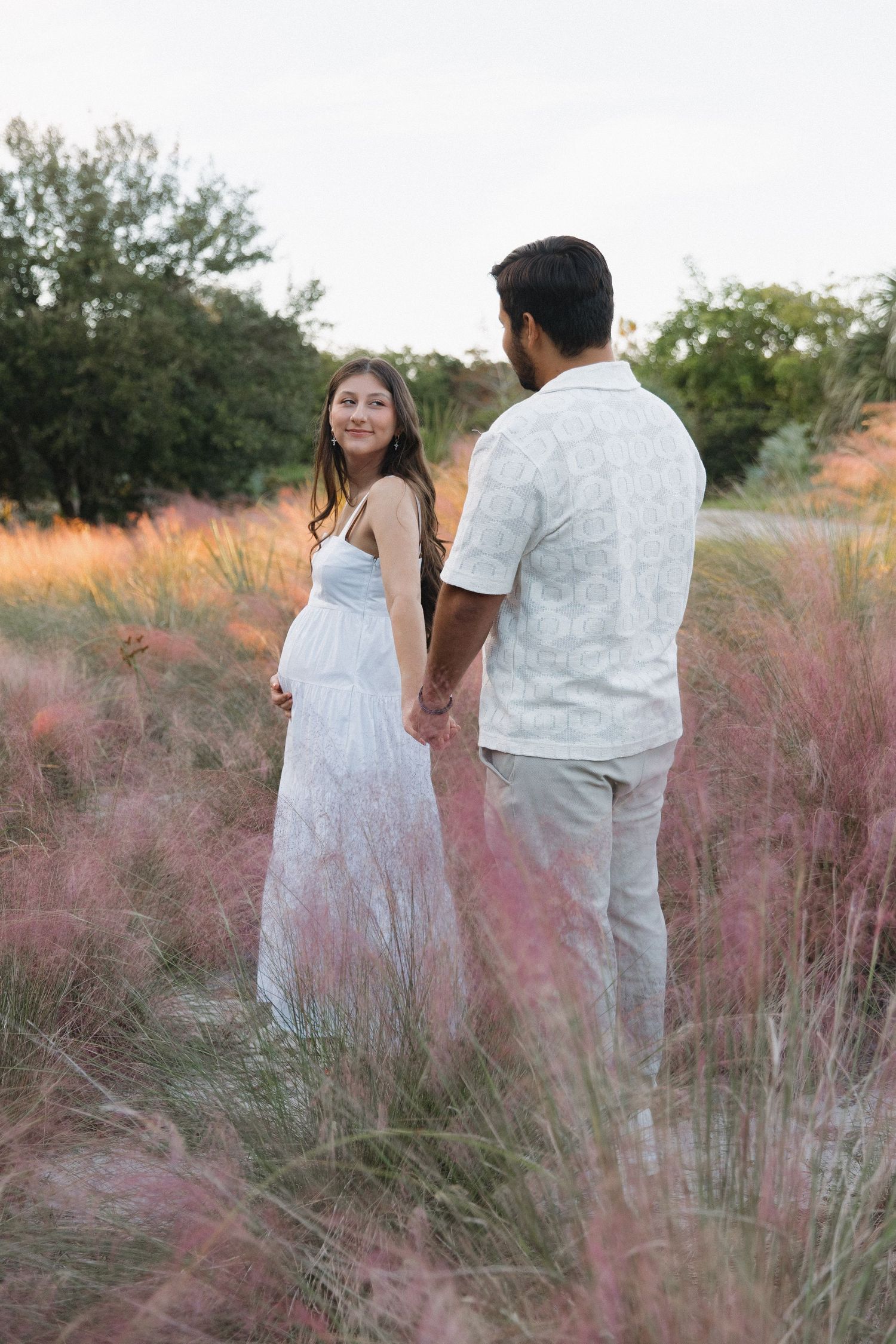 Couple walking through field of pink muhly grass at sunset.