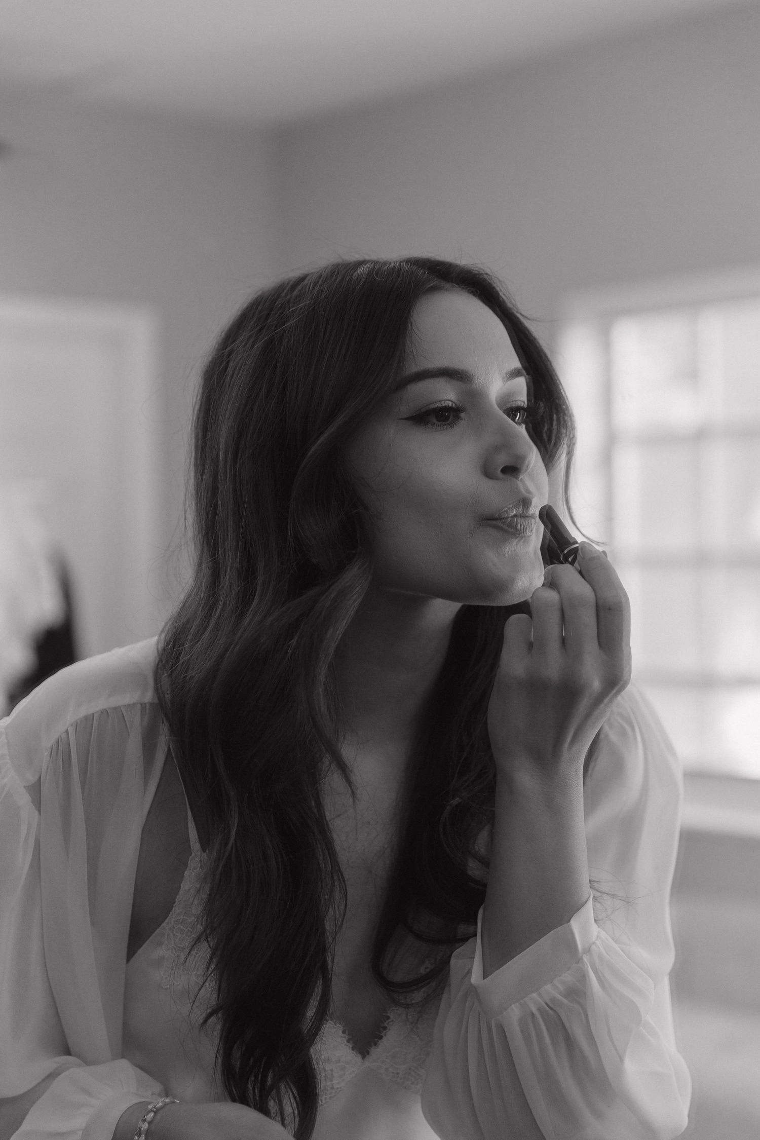 Black and white portrait of a person with long dark hair in a white blouse, gazing contemplatively with hand near face.