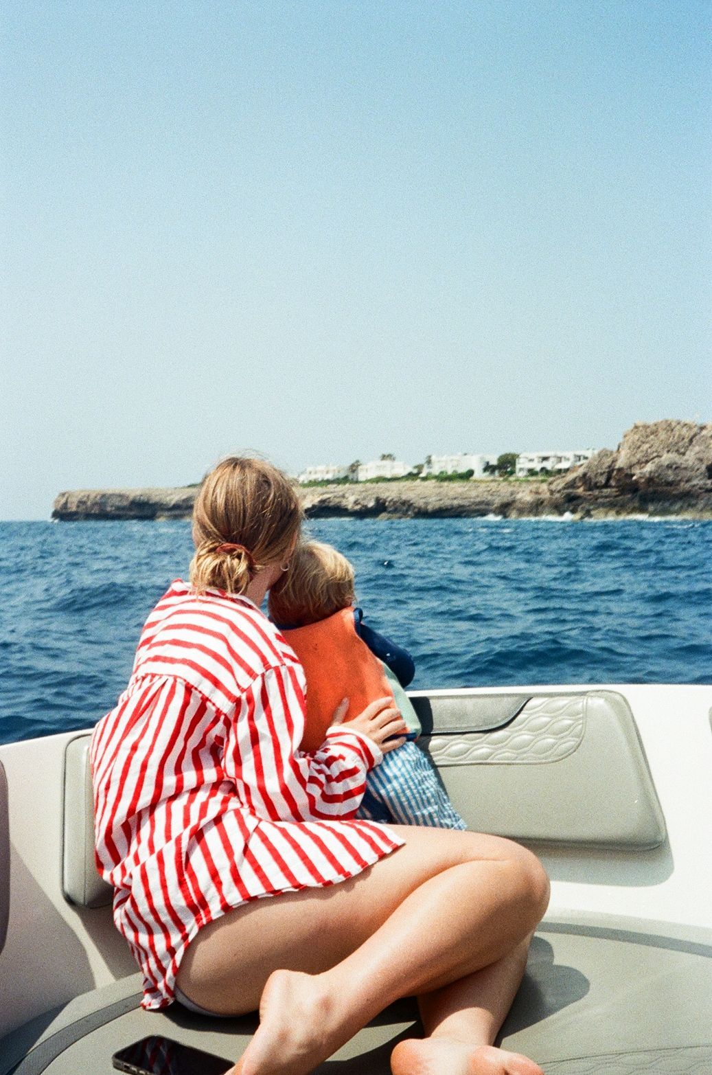 Person in red and white striped shirt lounging on boat with coastal cliffs in background.
