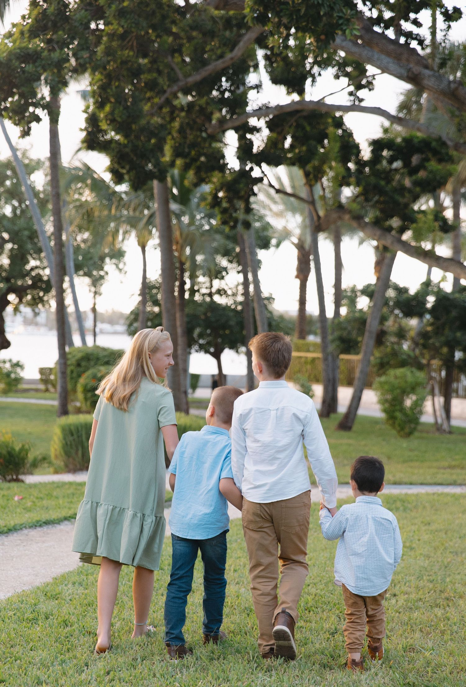 Family walking together on a tree-lined path through a peaceful park setting.
