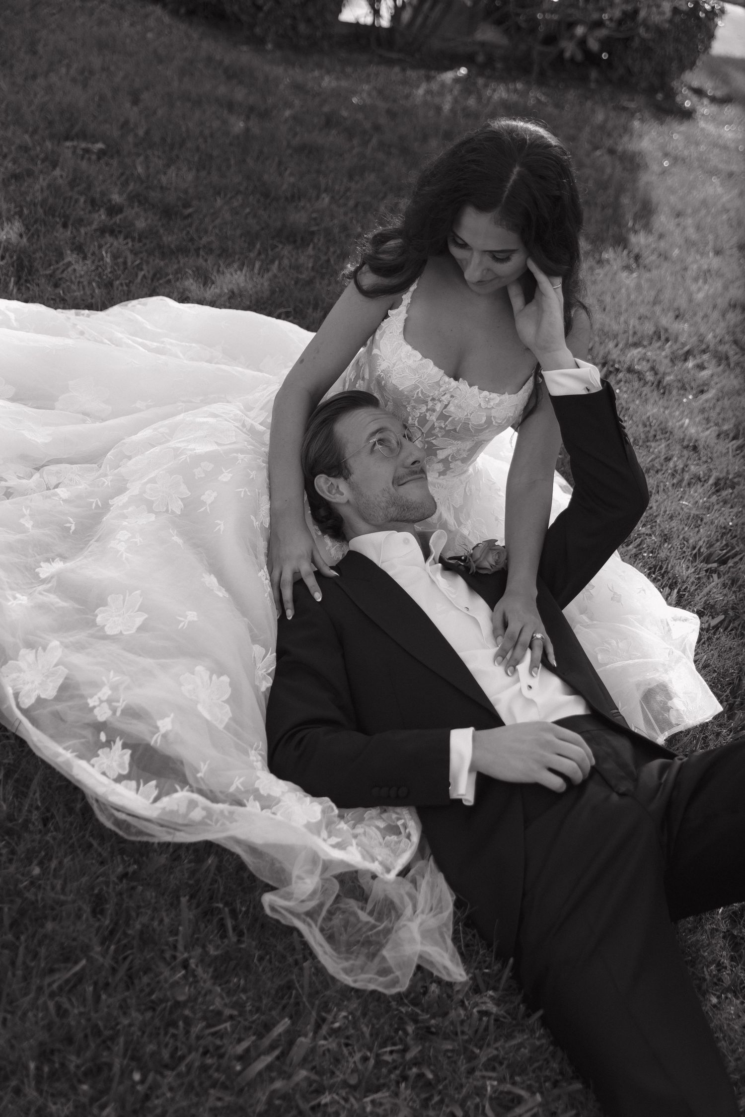 A couple lying in grass with a flowing white dress creating artistic black and white wedding portraits.