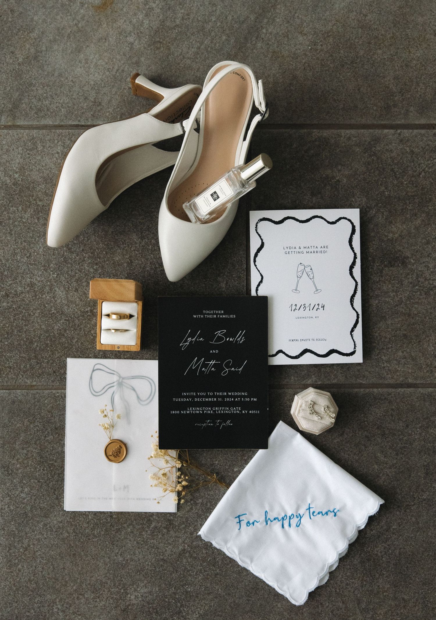 Elegant wedding details featuring white heels, invitations in black and white, and delicate accessories on gray concrete.