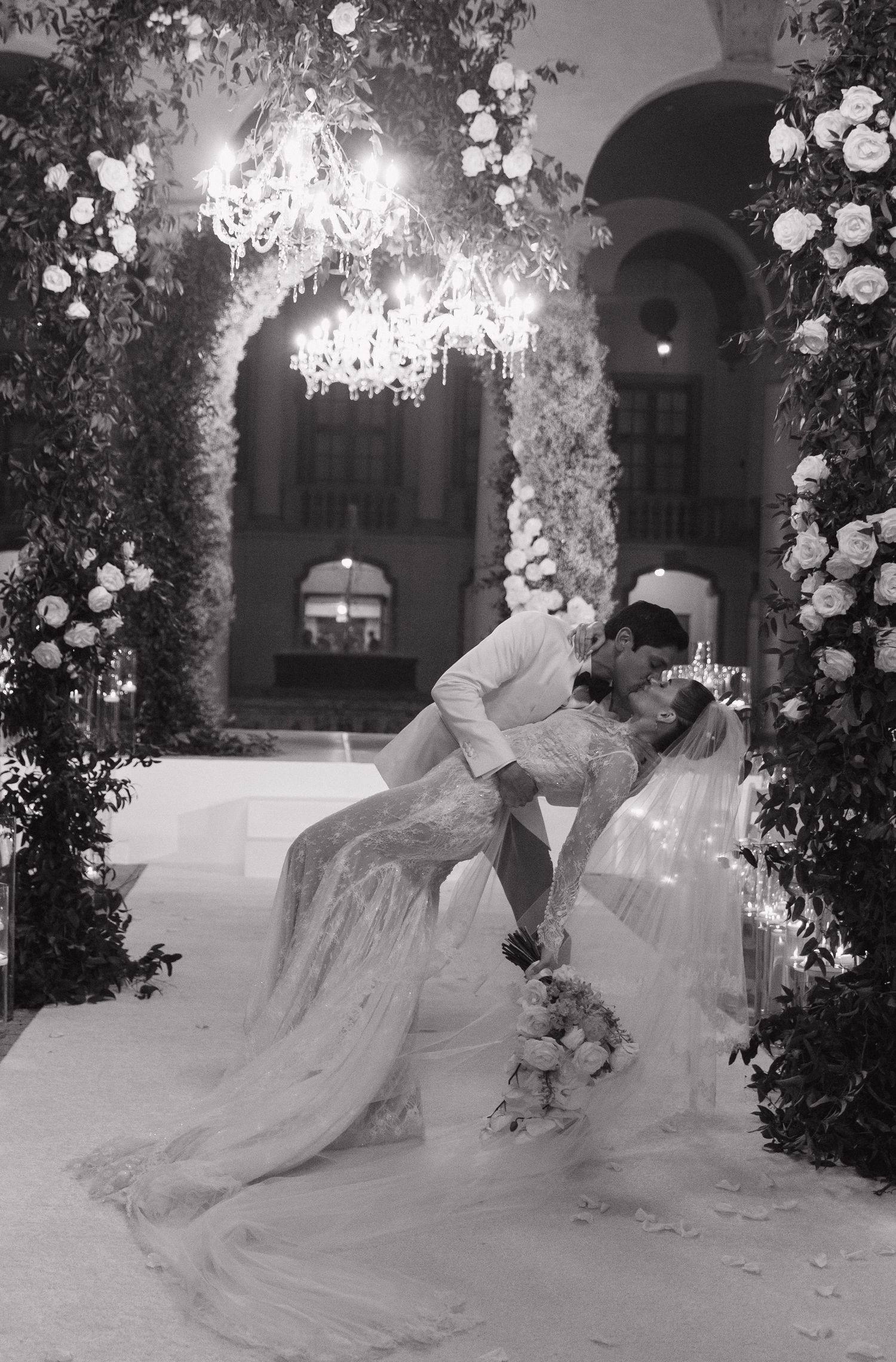 A romantic black and white photo series shows a couple in formal attire sharing a dip dance pose under floral decorations.