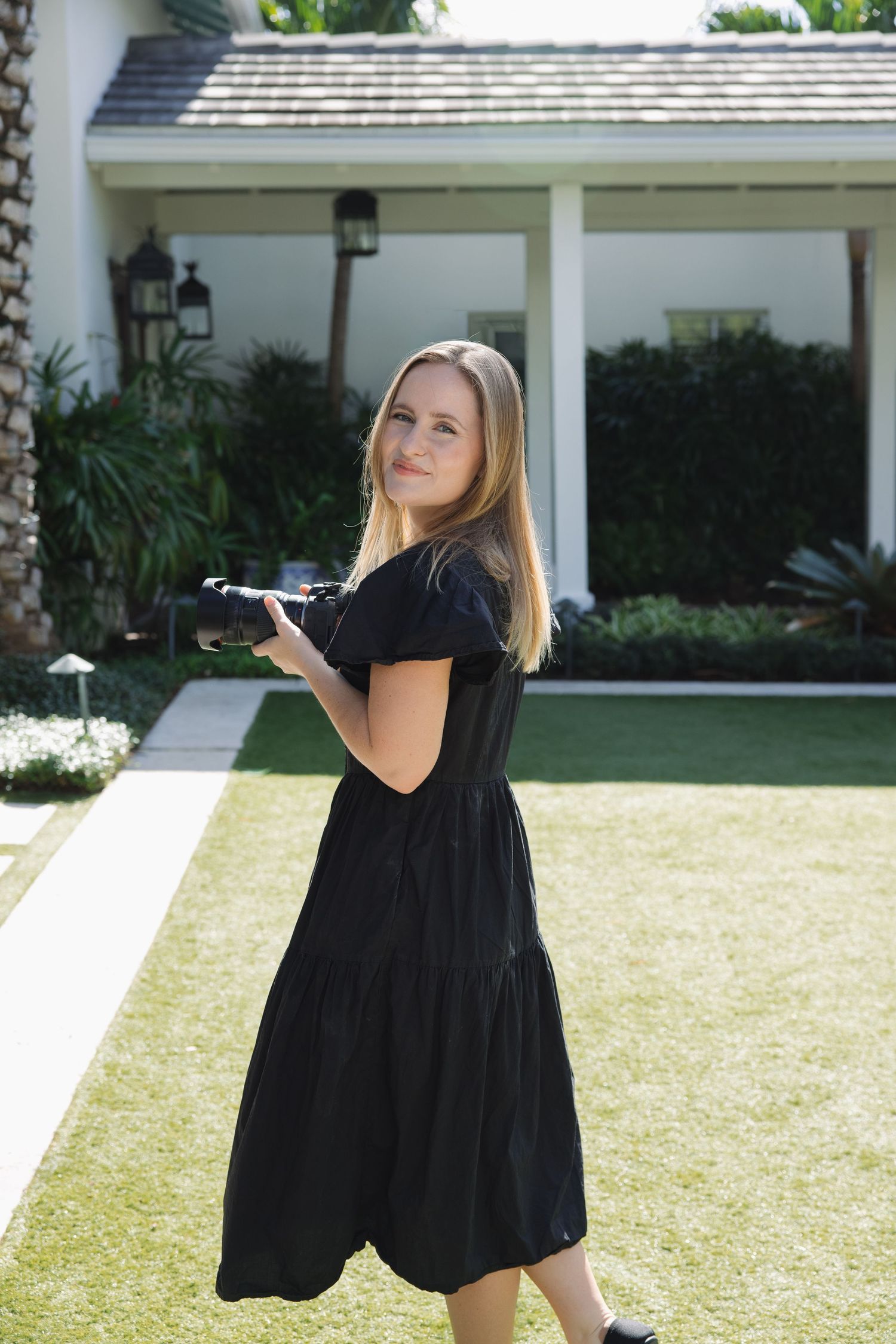 A sequence of images showing someone in a black dress twirling and dancing on a sunny lawn in front of a house.
