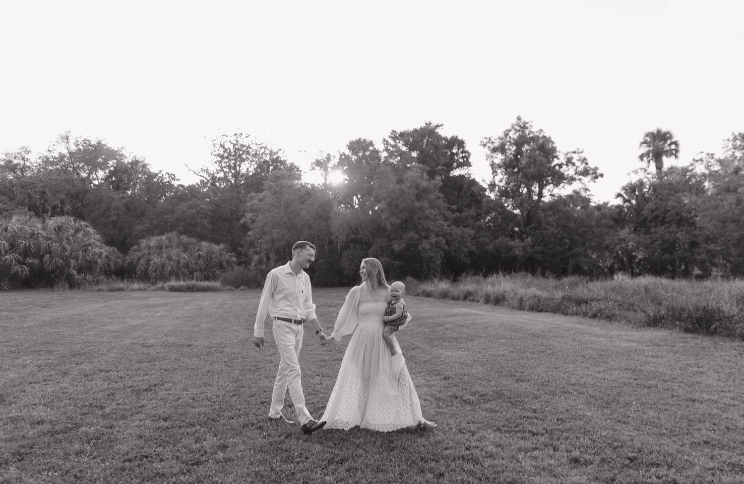 Couple walks together in an open field at sunset in black and white photography.