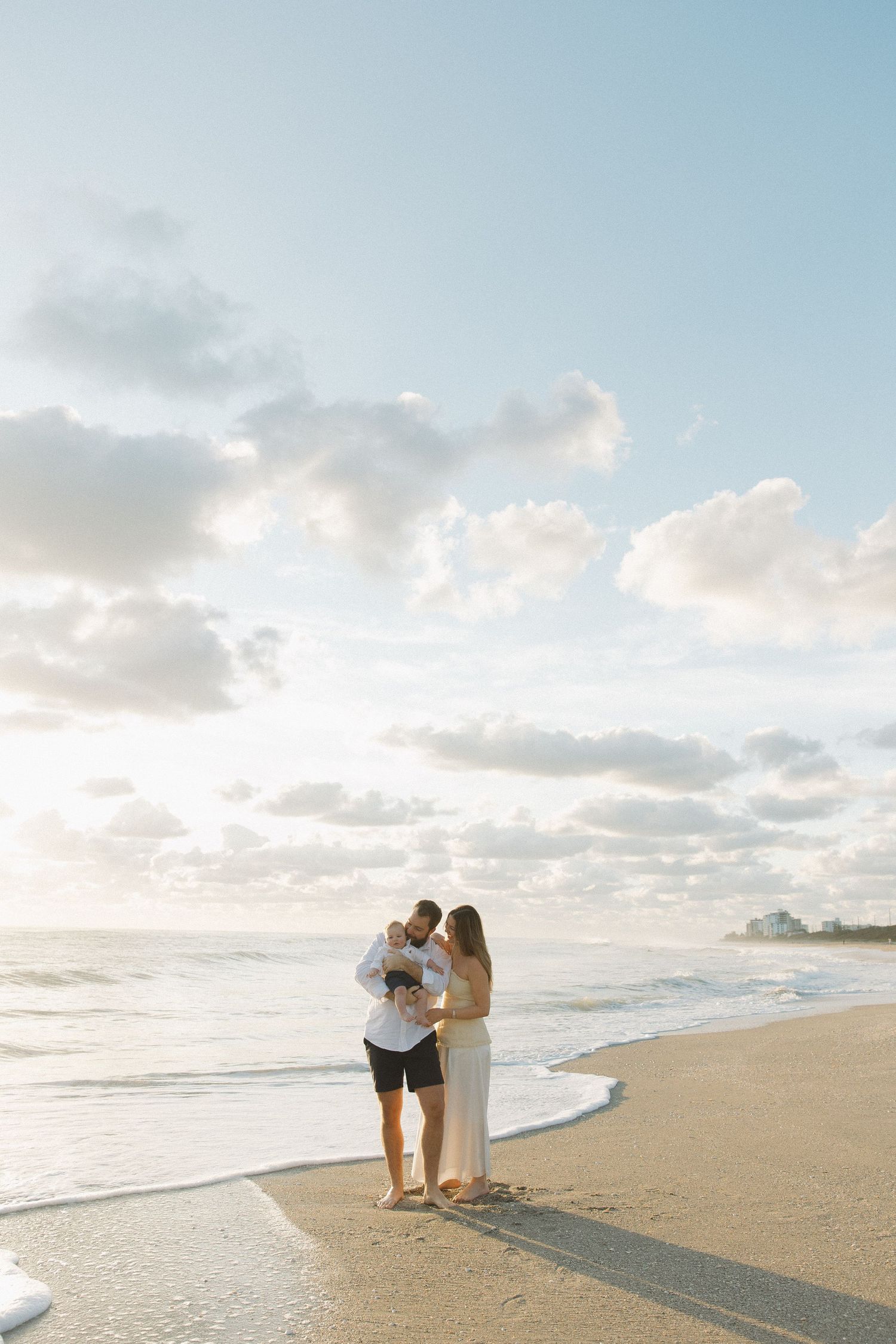 Two figures standing close together on a tranquil beach with gentle waves rolling in.