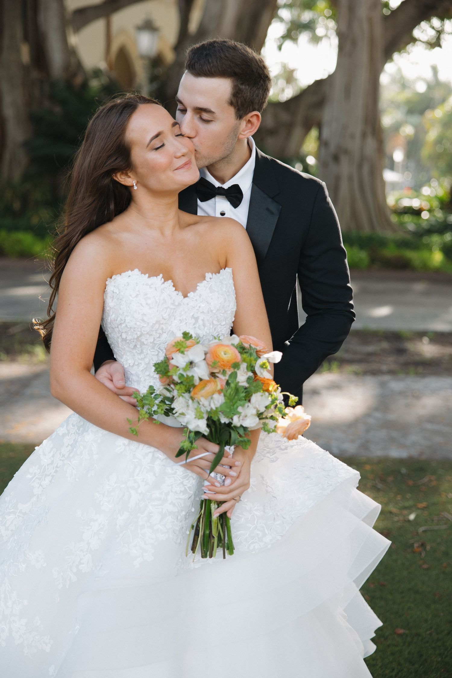 Romantic wedding couple poses in a scenic garden setting with lace white gown and black tuxedo.