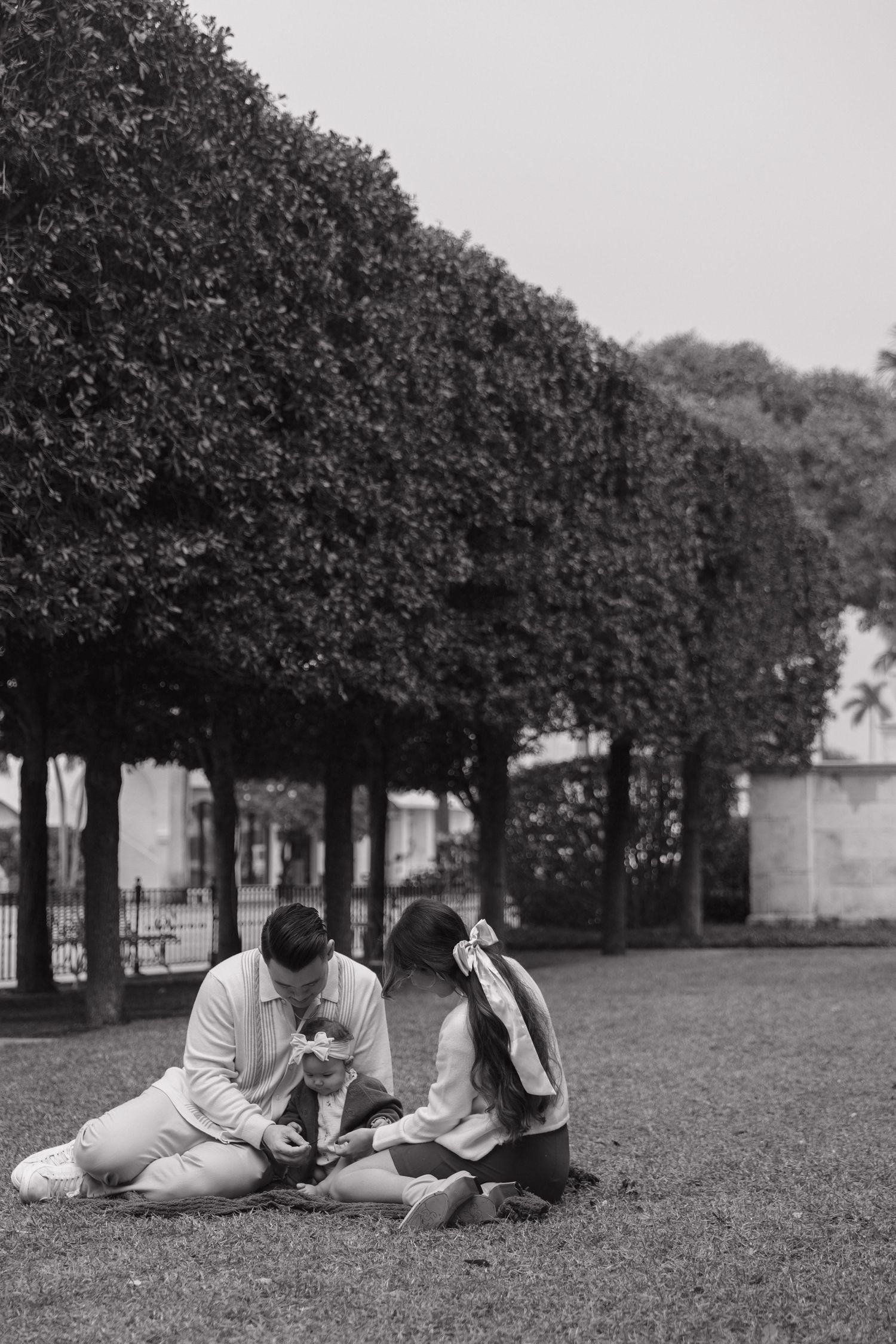 Family enjoying a picnic together while lying on grass under trees in a park.