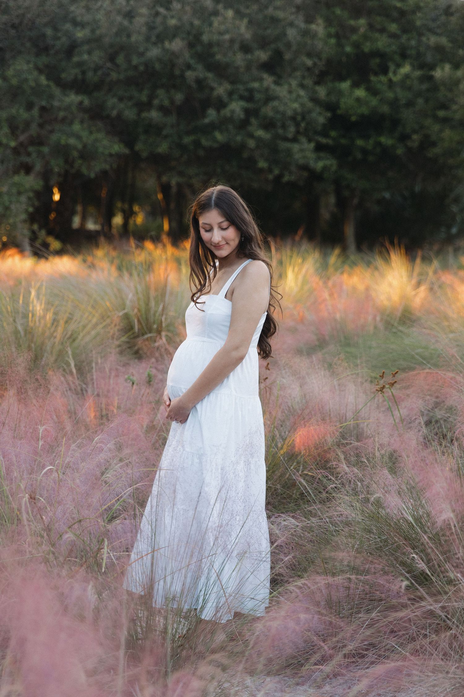 Woman in white dress walking through tall pink muhly grass at golden hour.