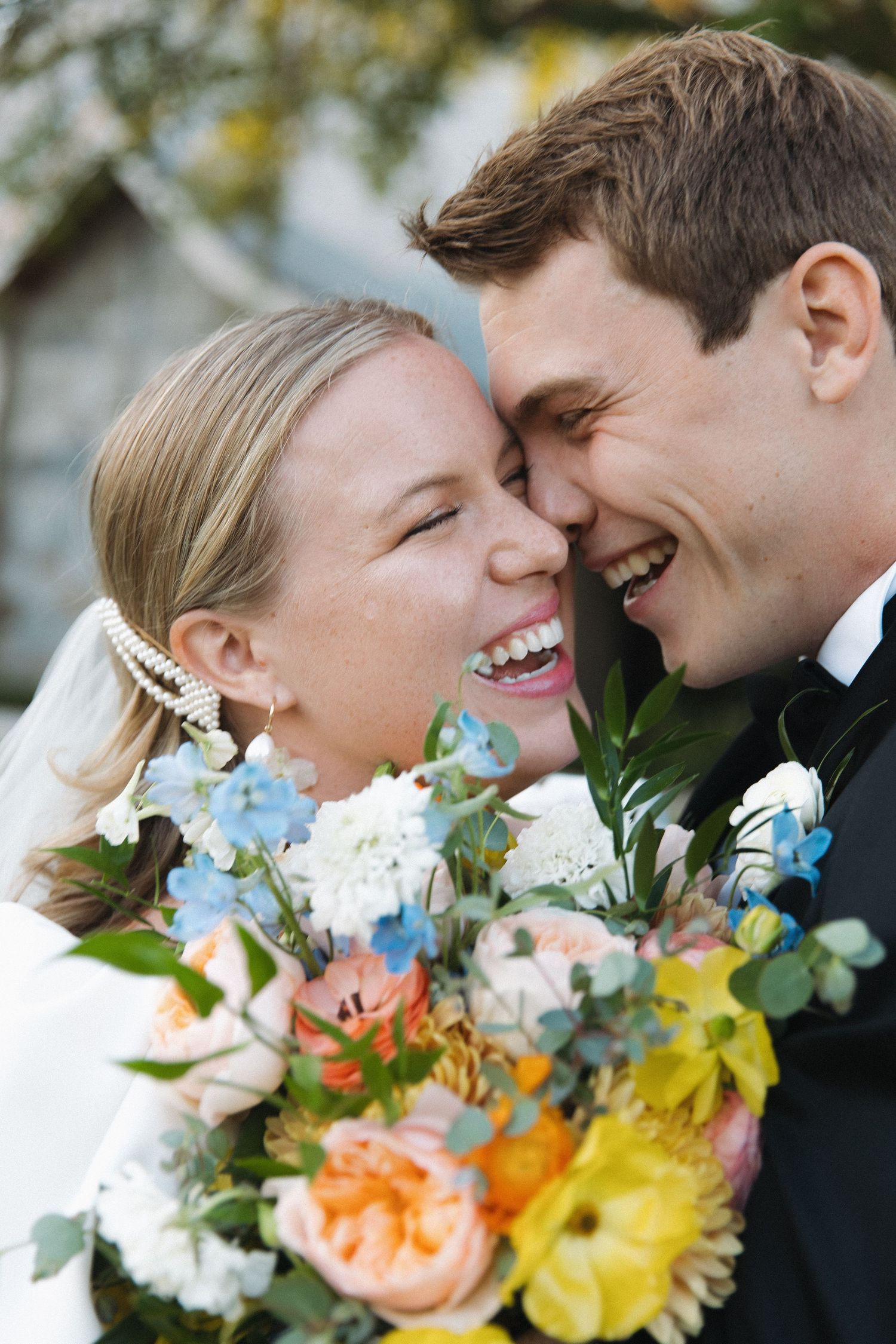 A joyful couple share a laughing moment while holding a vibrant bouquet of flowers at their wedding celebration.