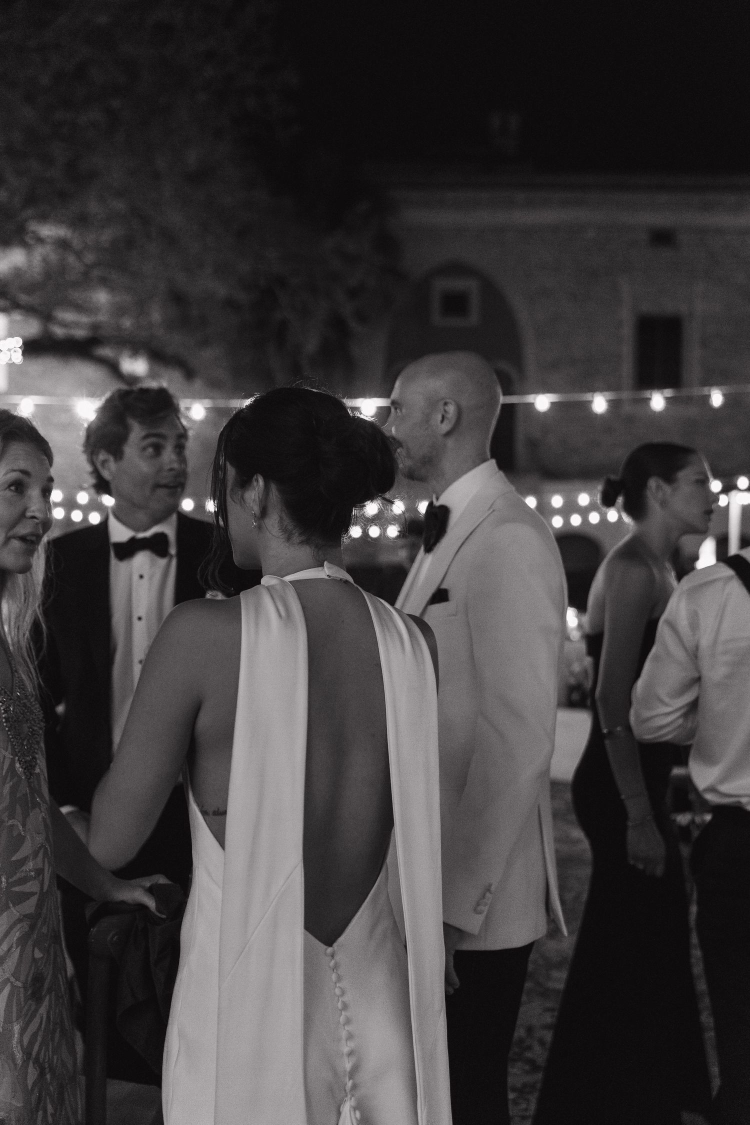 Black and white photo of an elegant evening party with string lights and formal attire.