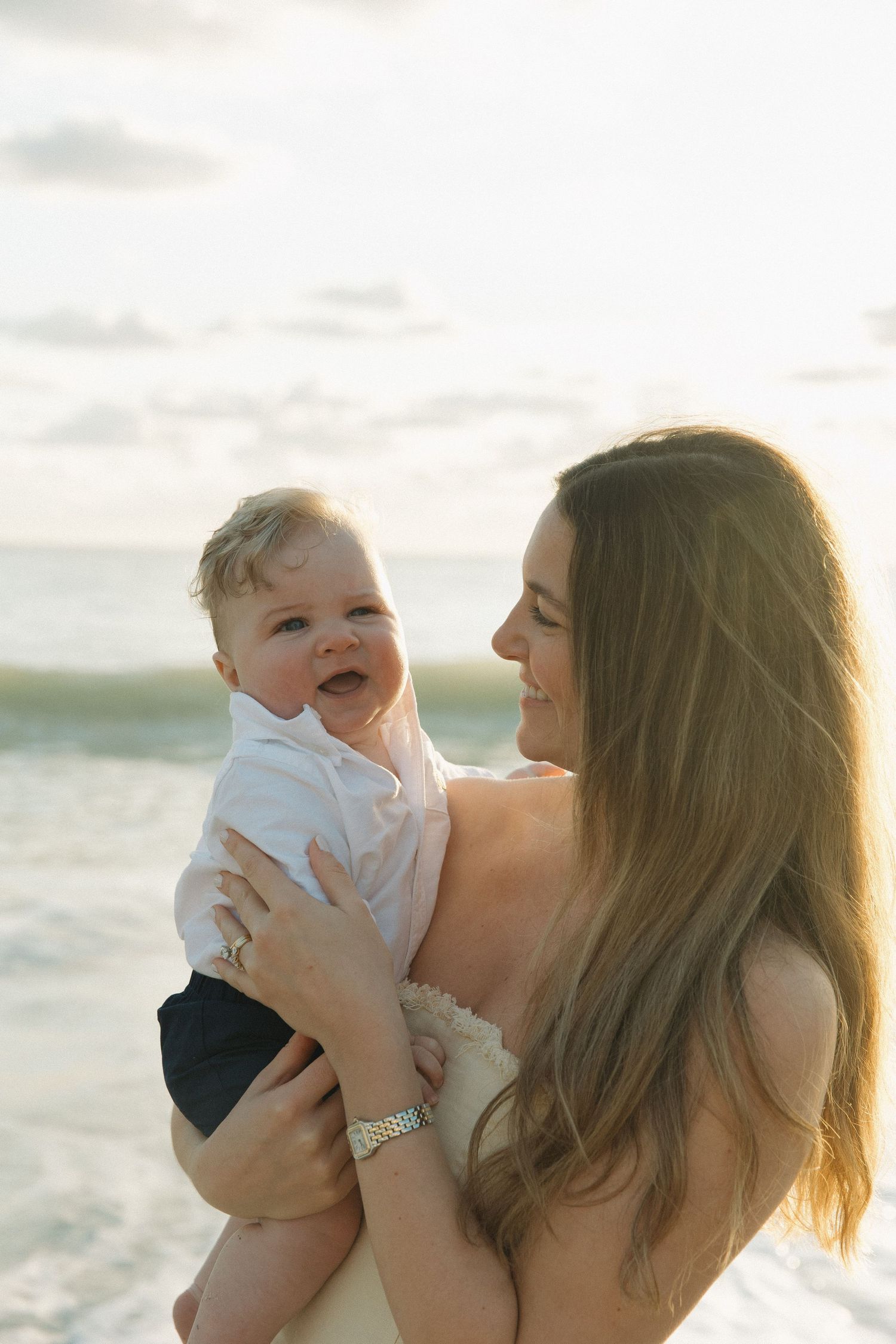 Tender moment between parent and baby captured against ocean backdrop at sunset.