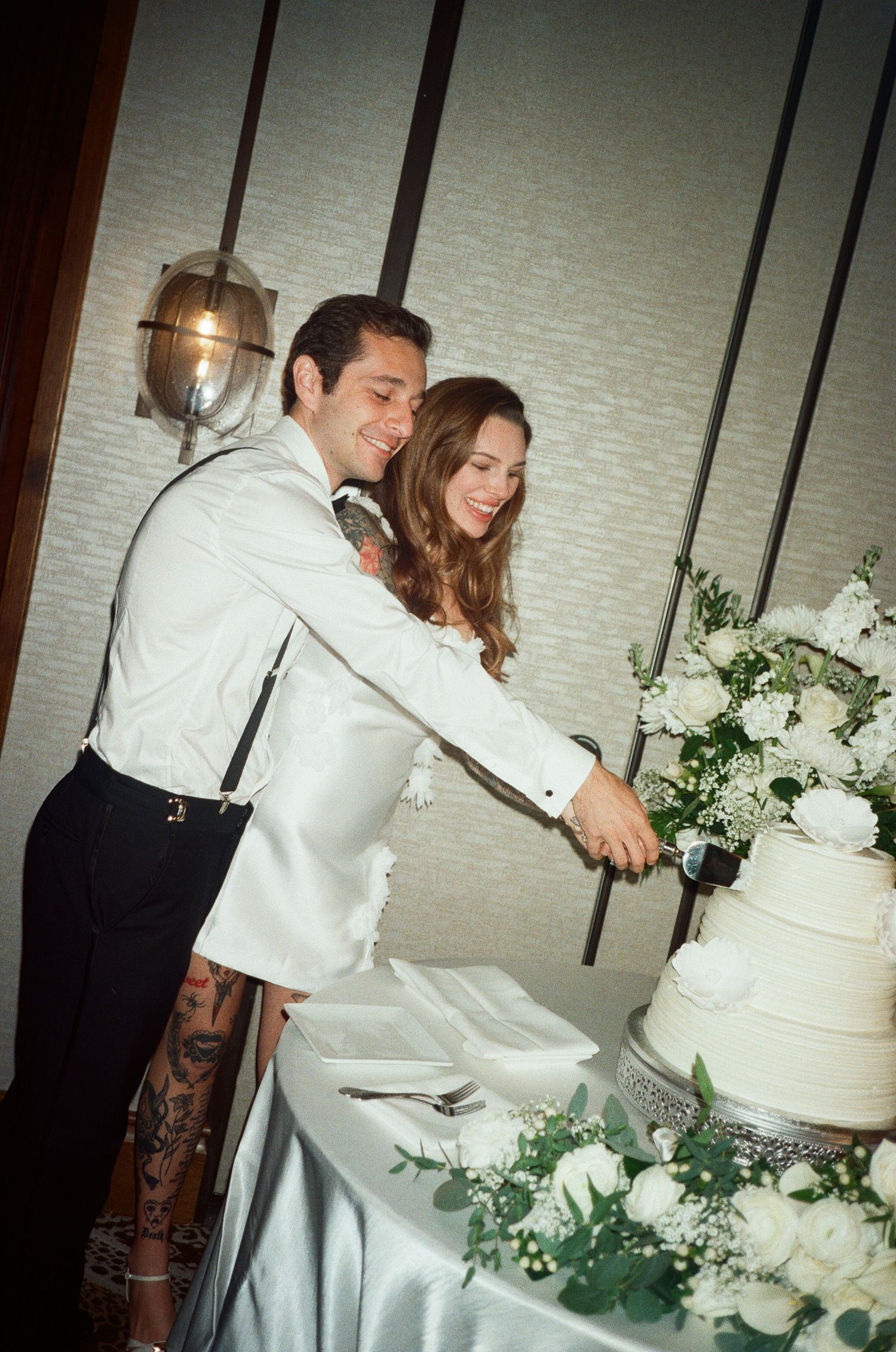 A couple cuts their elegant white wedding cake decorated with fresh flowers at their reception.