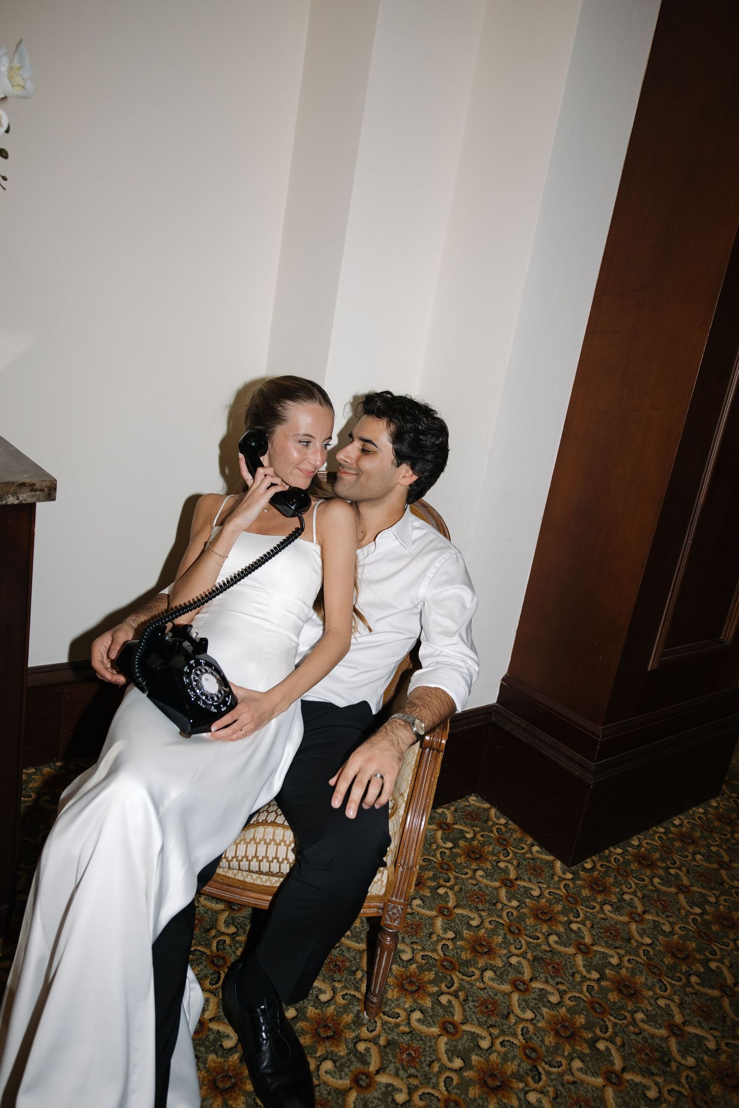 A couple shares intimate moments on patterned carpet in an indoor setting with white walls.