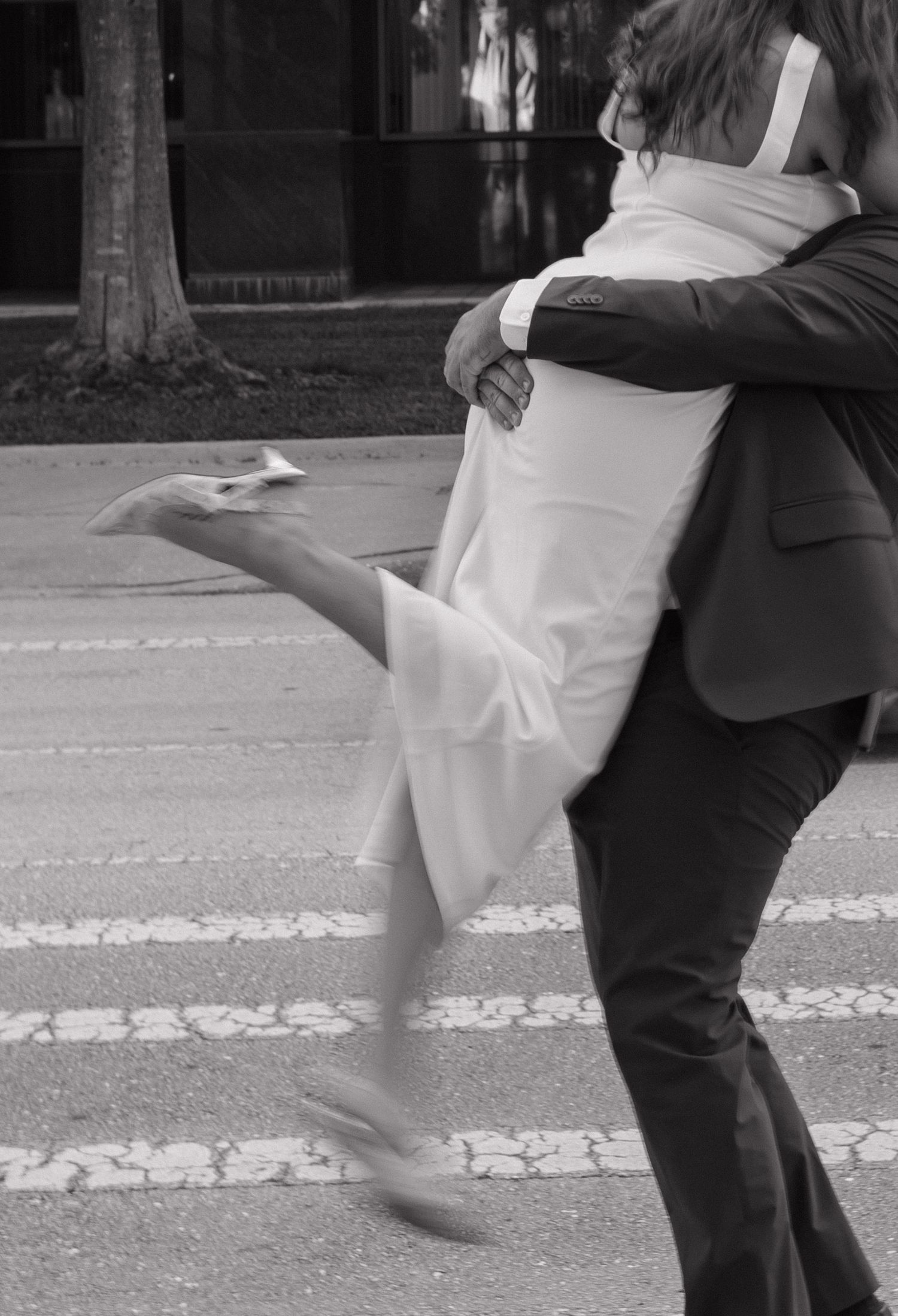 A black and white photograph captures a romantic embrace and dance move on a crosswalk.