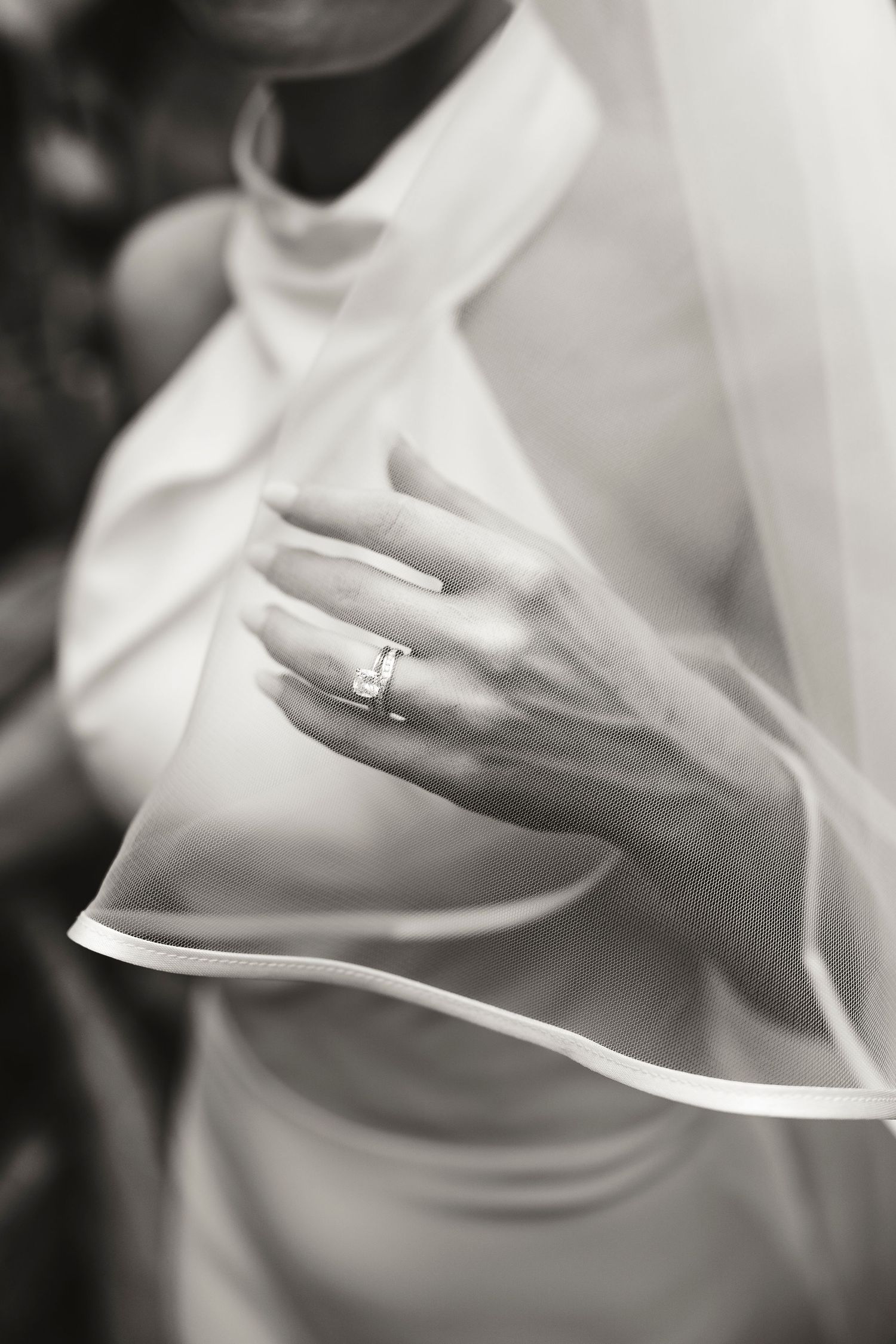 Black and white close-up of a bride's hand wearing a diamond engagement ring, holding her wedding veil.