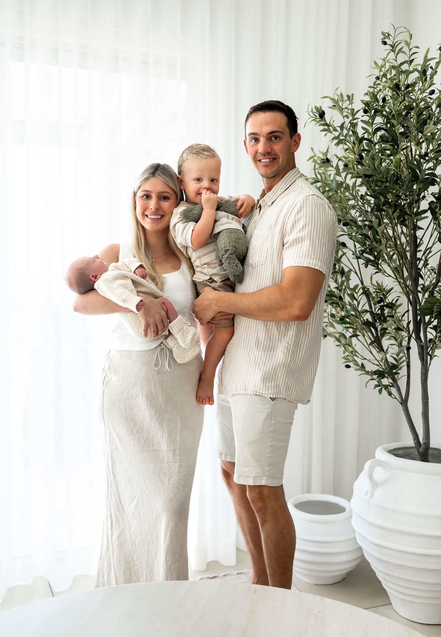 Happy family of four posing together with newborn and toddler in white outfits.