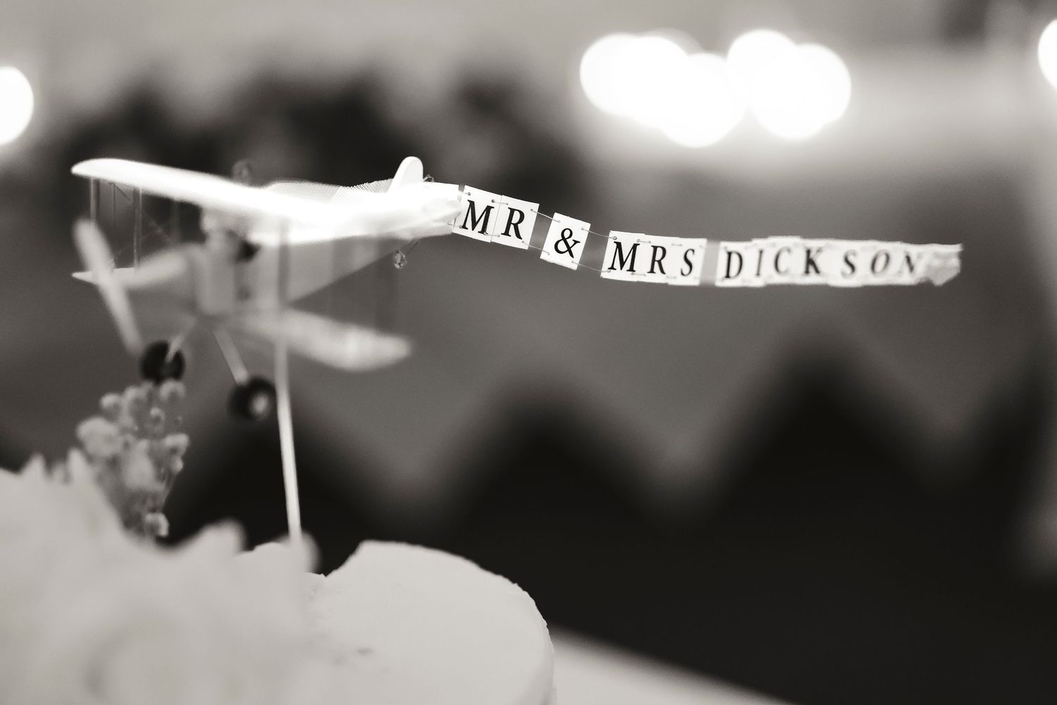 Black and white wedding cake topper featuring a toy airplane with Mr & Mrs Dickson banner sign.