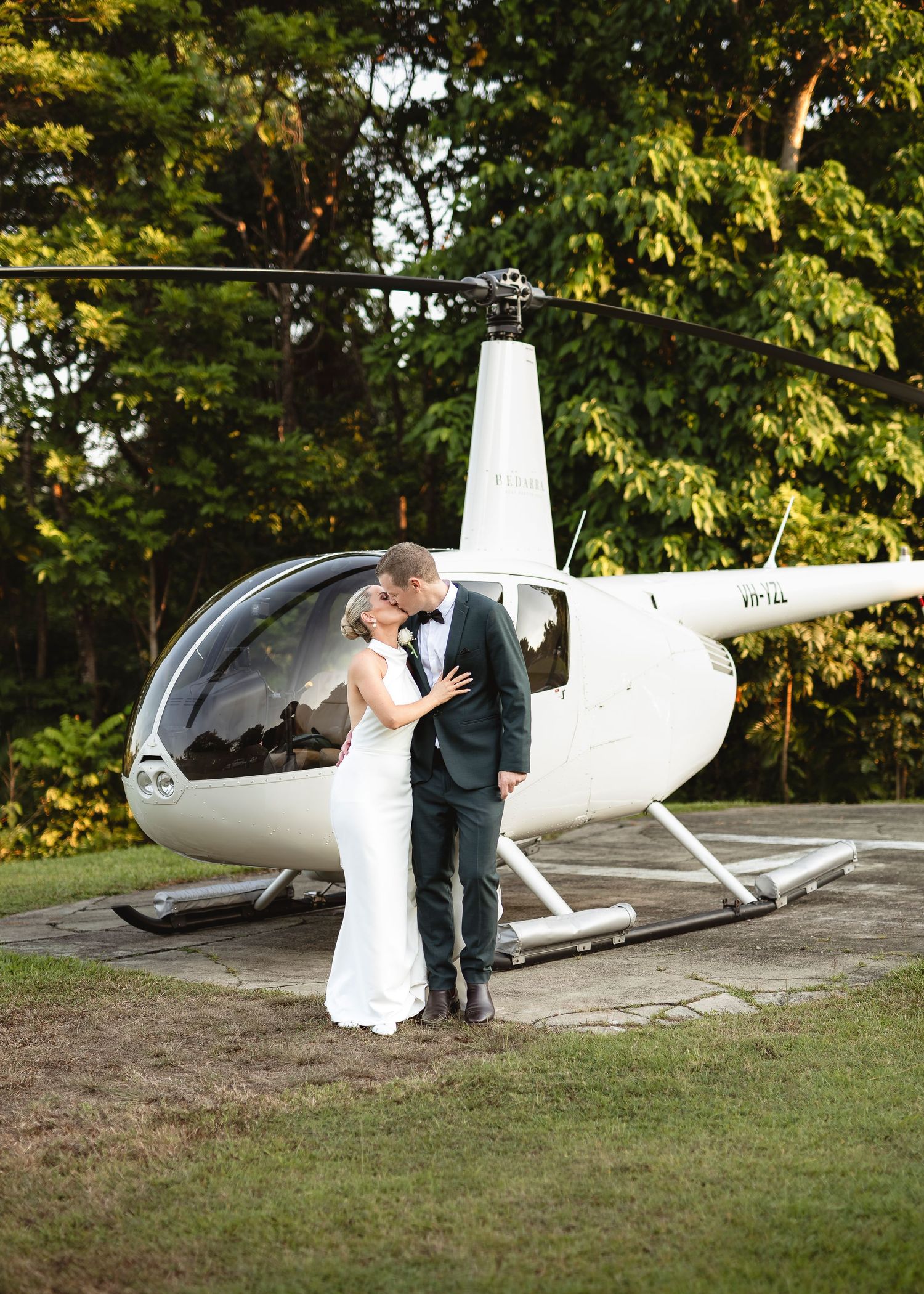 A bride and groom share a romantic kiss in front of a white helicopter on their wedding day.