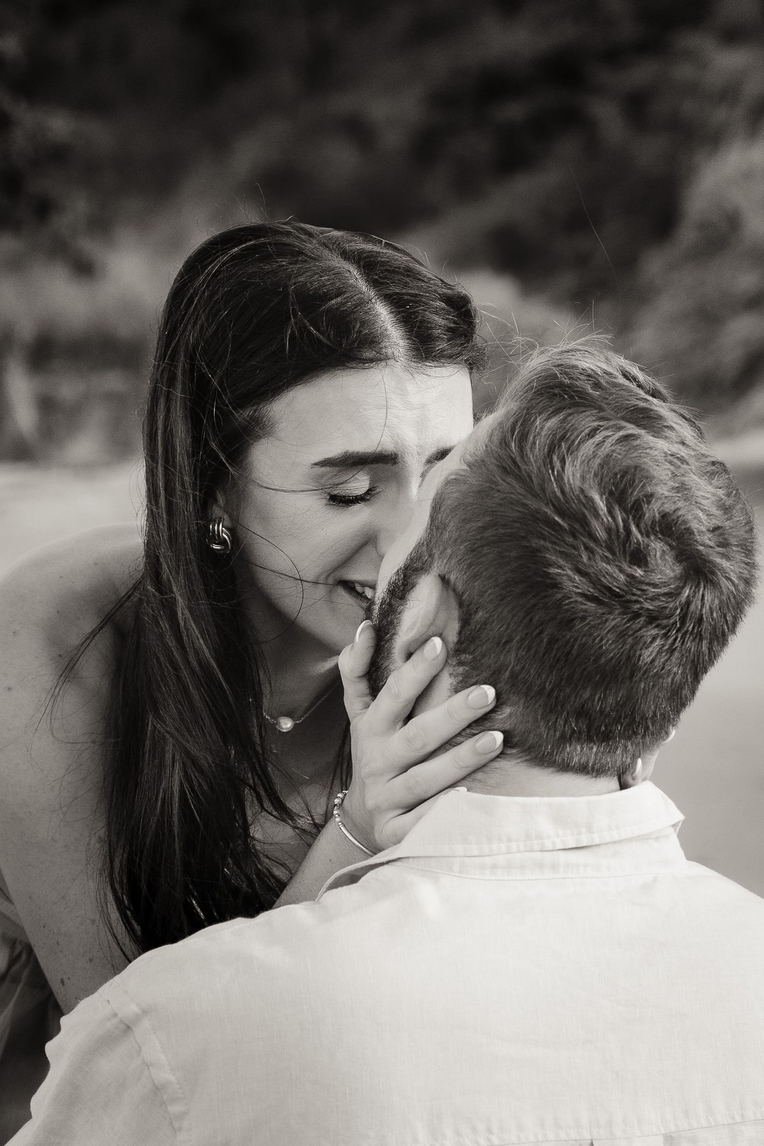 Black and white photo of a couple sharing a tender kiss outdoors, woman gently holding mans face.