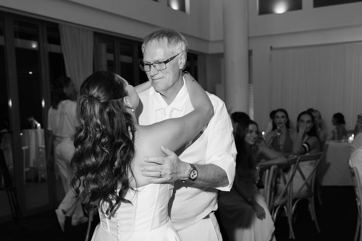 Black and white photo of a bride and older man sharing an emotional father-daughter dance at a wedding reception.