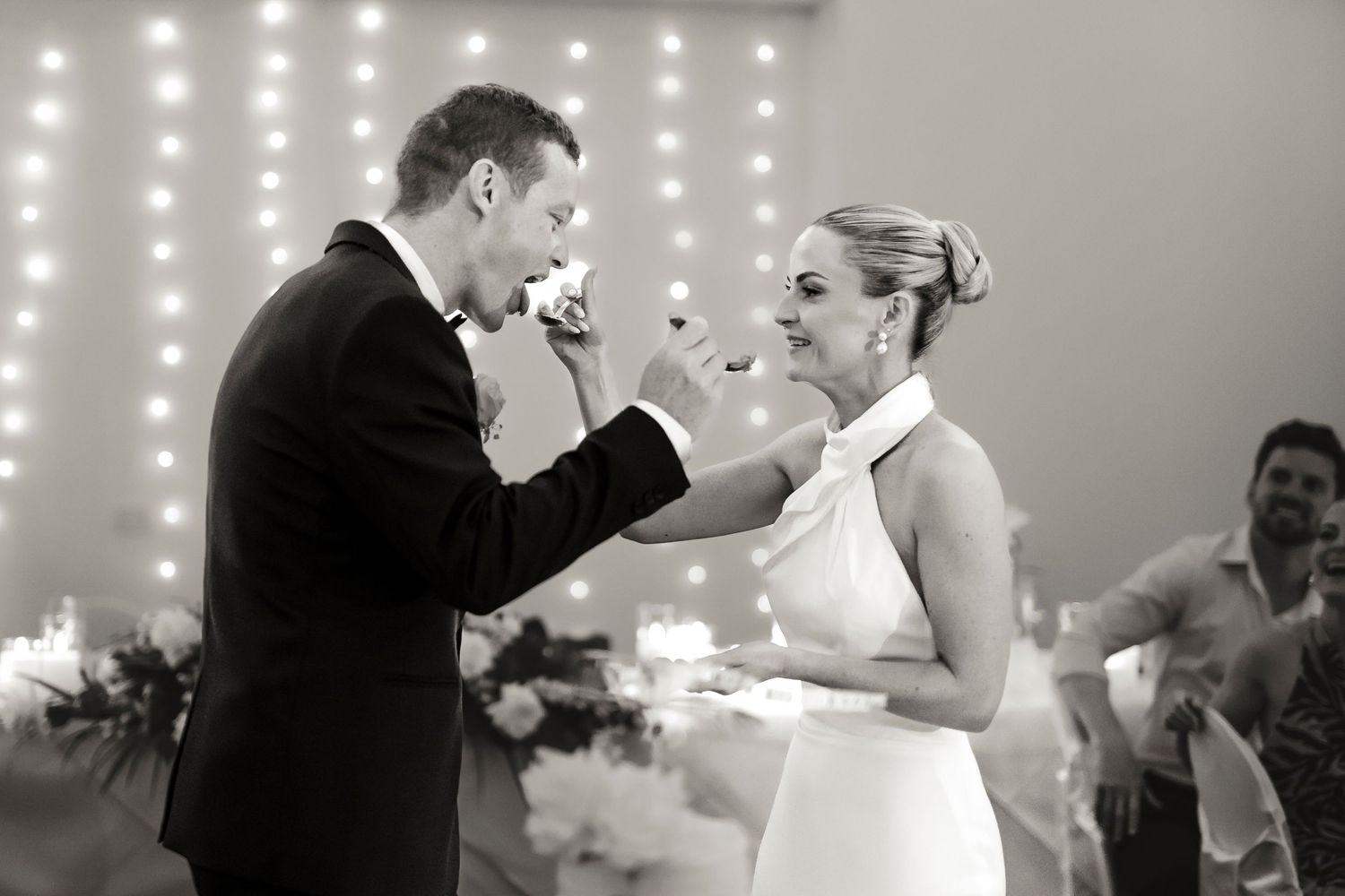 Black and white photo of bride and groom sharing wedding cake during reception celebration.