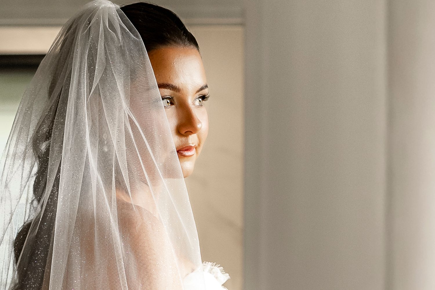 A beautiful bride wearing a delicate white veil, smiling softly in elegant bridal attire on her wedding day.