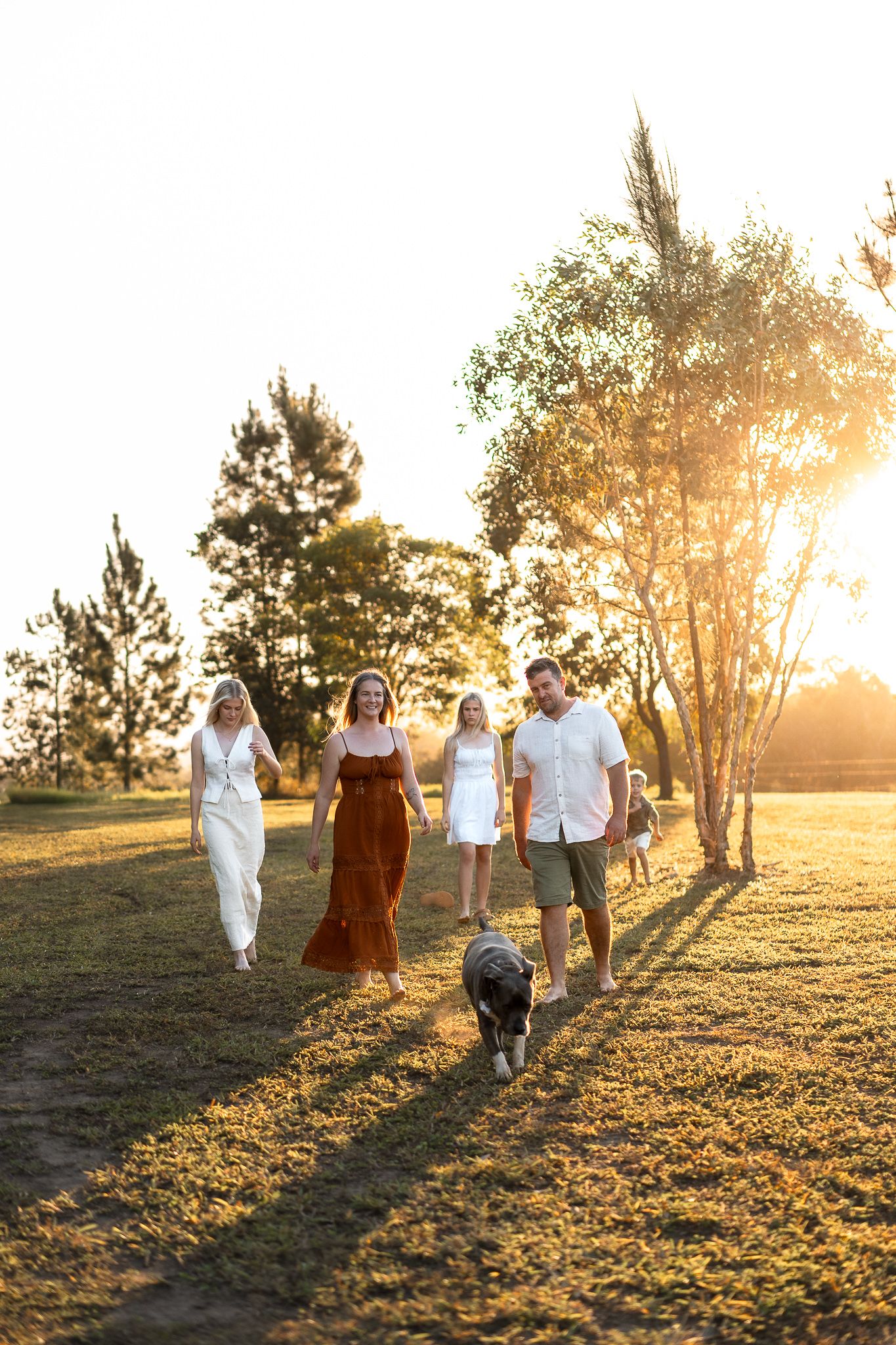 Family with dog walking through sunlit park at golden hour with long shadows.