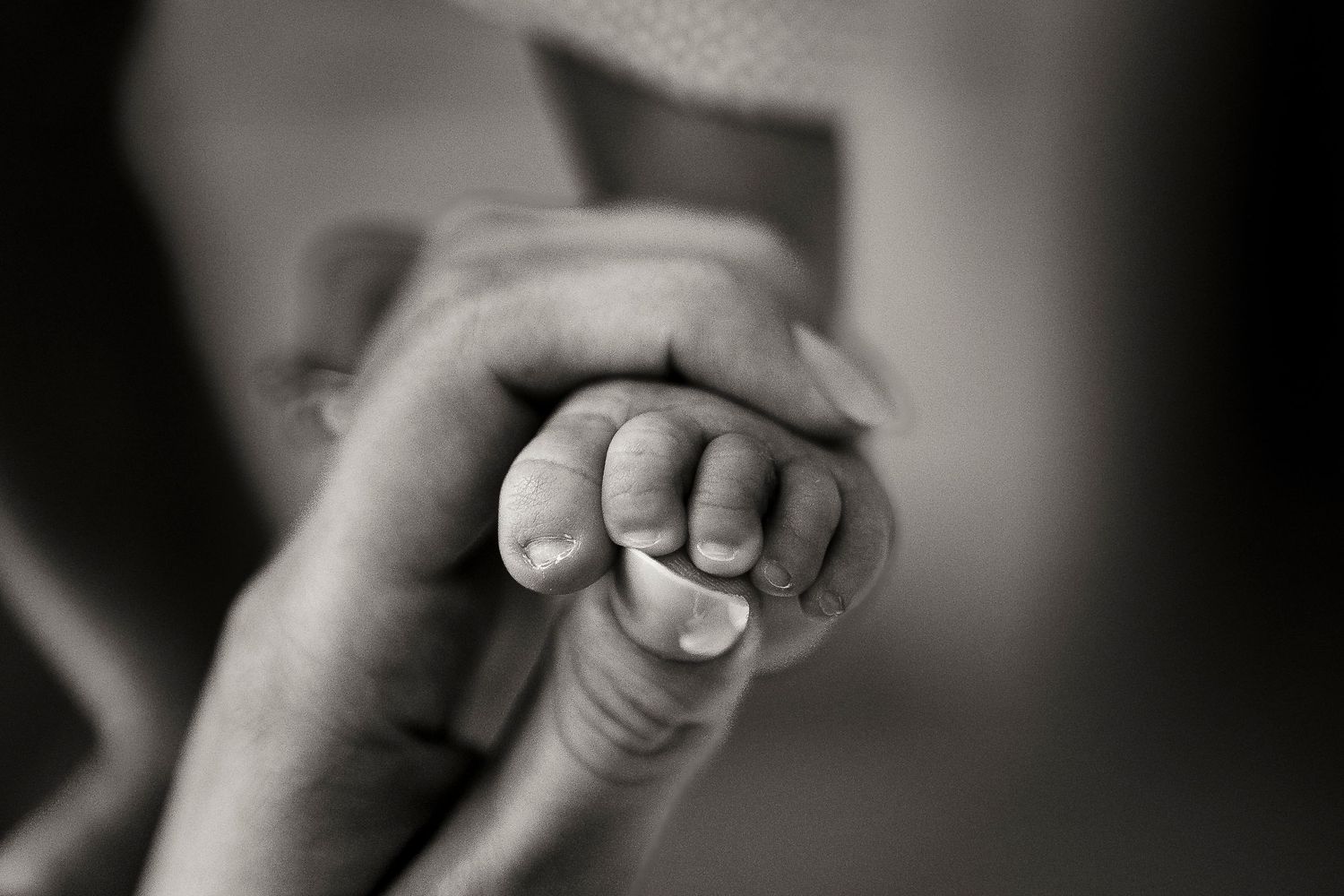 Black and white close-up of a newborn baby gripping an adult's finger.