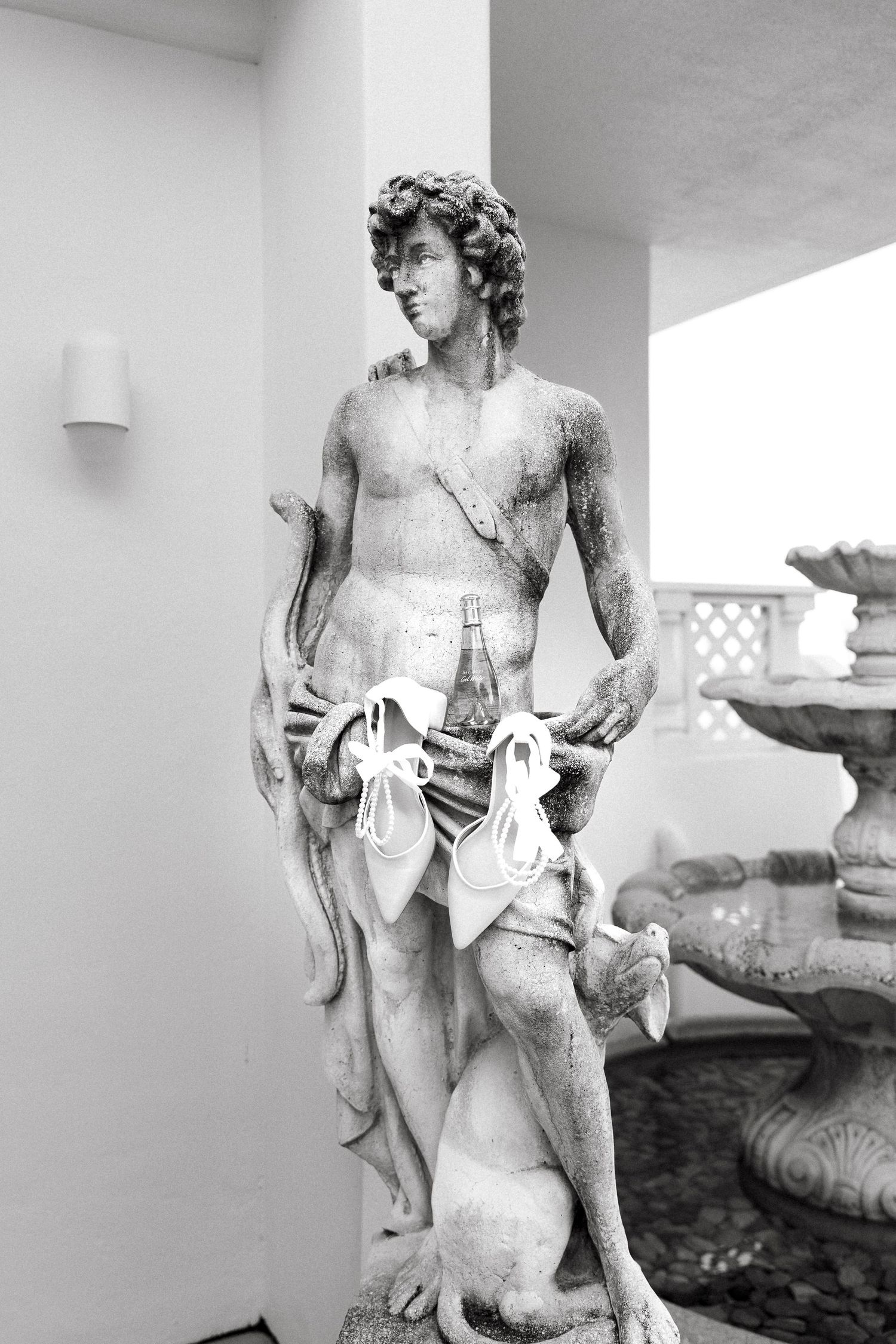 Black and white photo of a classical male statue decorated with wedding accessories.