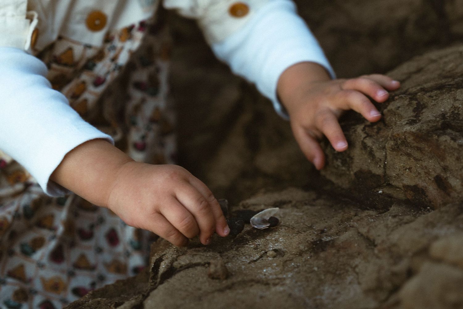 Close-up of a young child's hands exploring and touching a rough rocky surface outdoors.