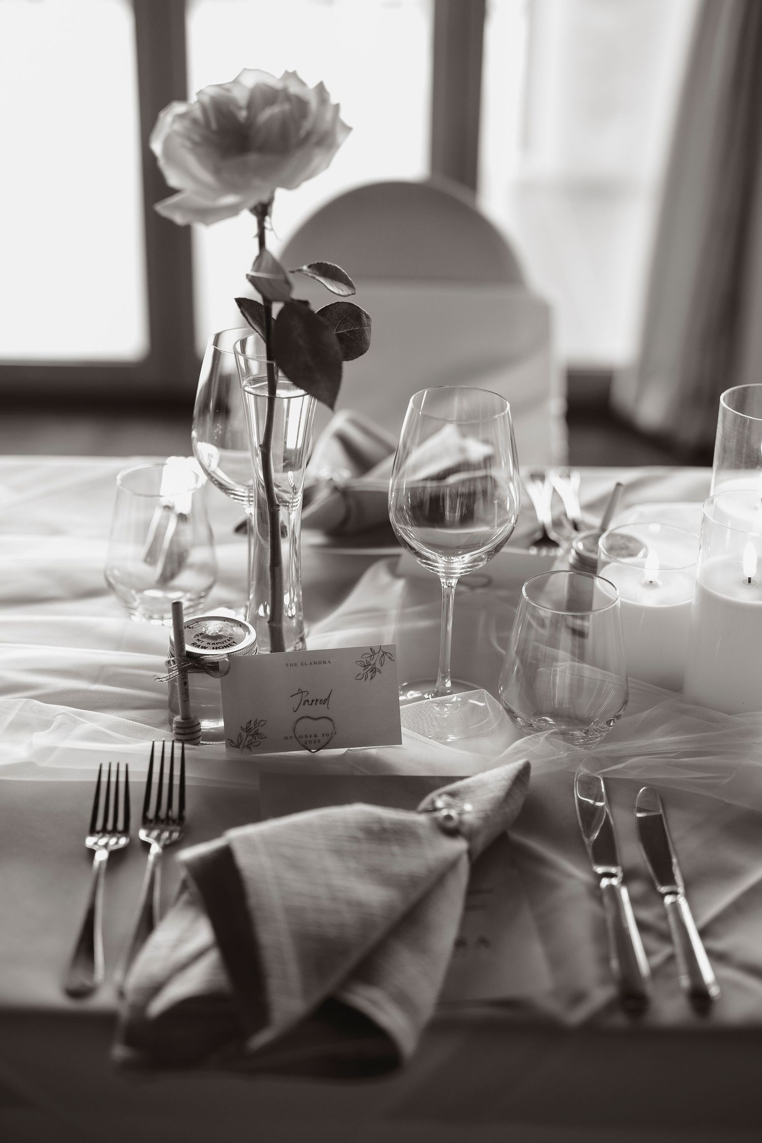Elegant black and white wedding table setting with wine glasses, folded napkins, silverware, and a single rose centerpiece.