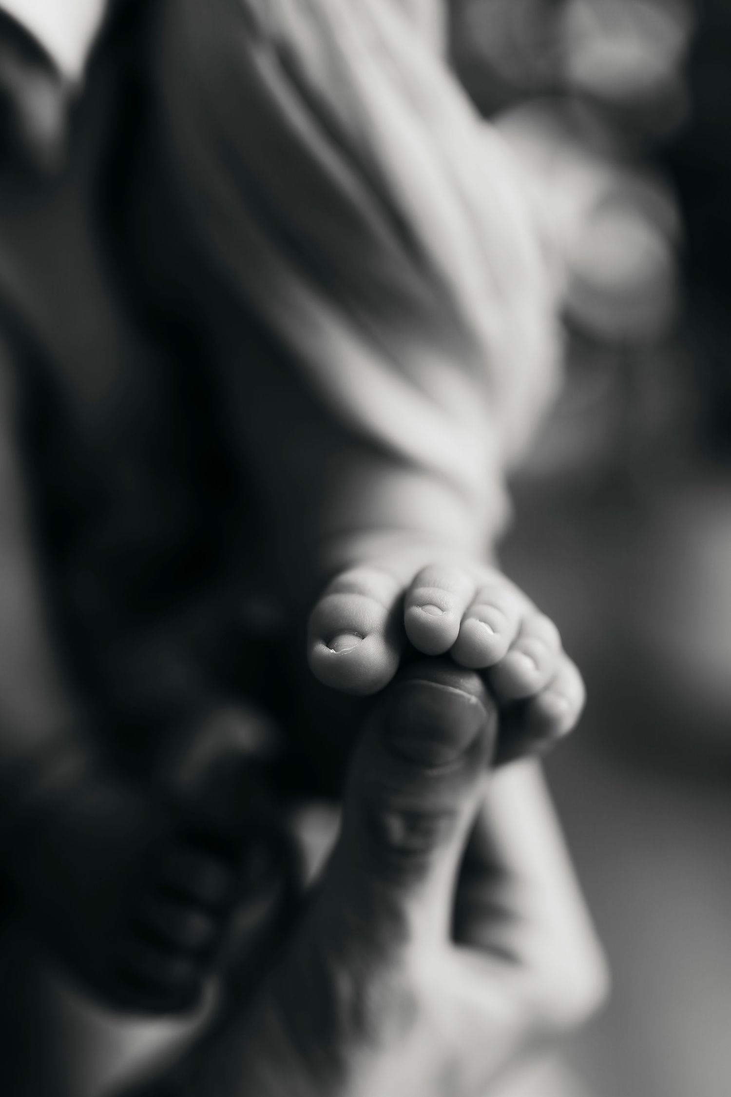 Black and white close-up of newborn baby tiny feet held by parent's hand.