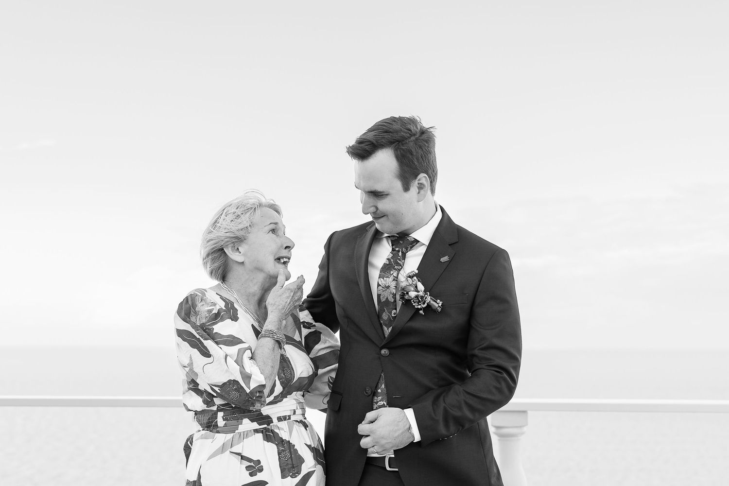 Black and white photo of a laughing bride and groom sharing a joyful moment outdoors on their wedding day.